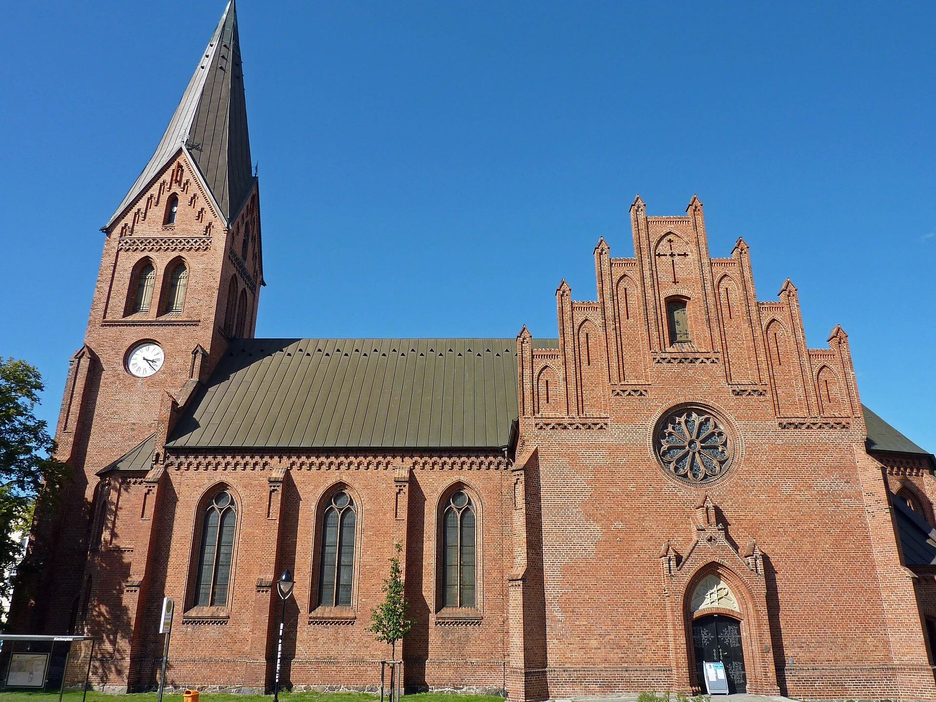 Neugotische Backsteinkirche von Warnemünde mit Turm, Staffelgiebel und Rosettenfenster bei blauem Himmel.