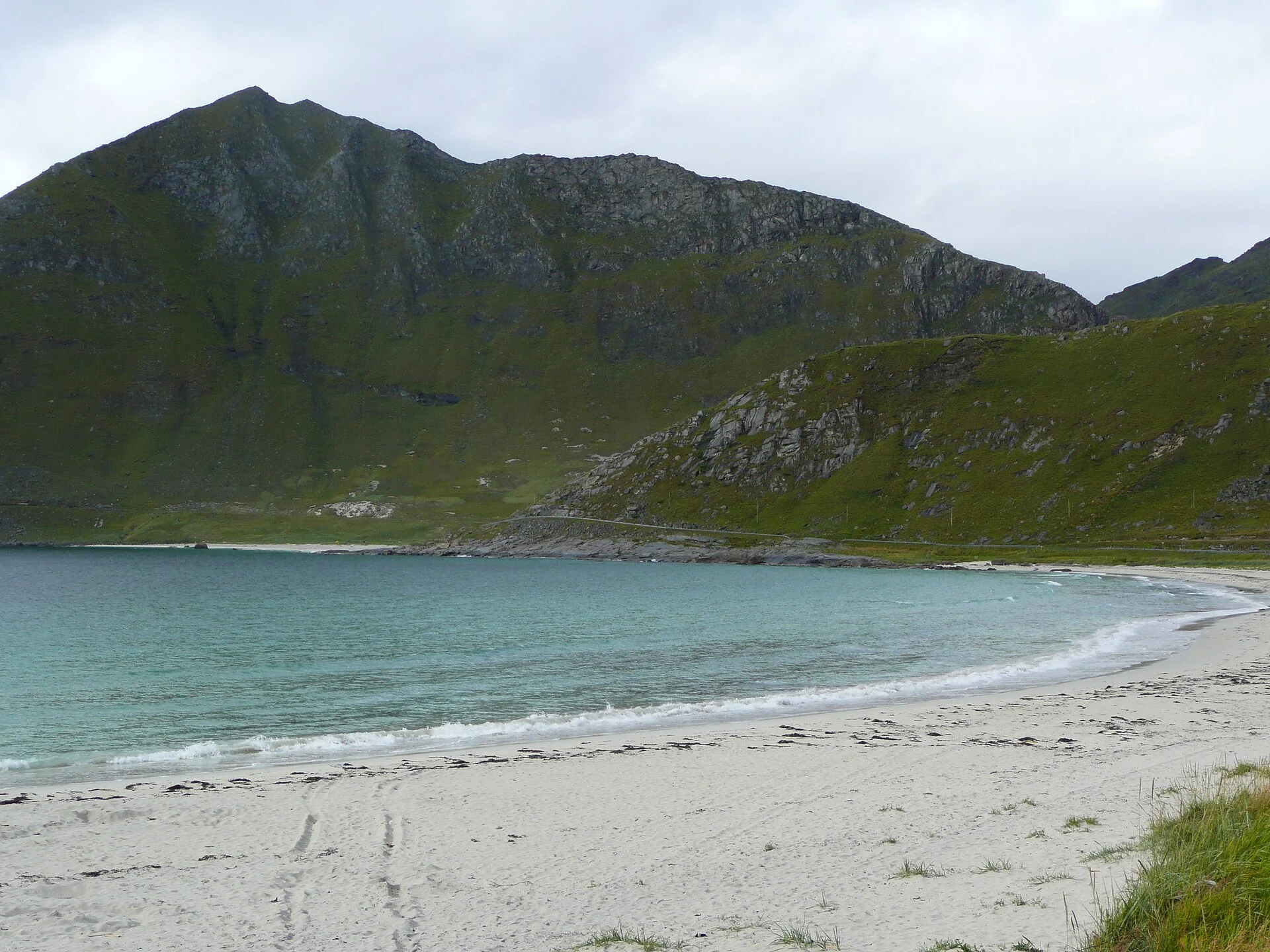 Heller Sandstrand mit türkisem Wasser und steil aufragenden Bergen am Haukland strand bei Leknes, Lofoten.