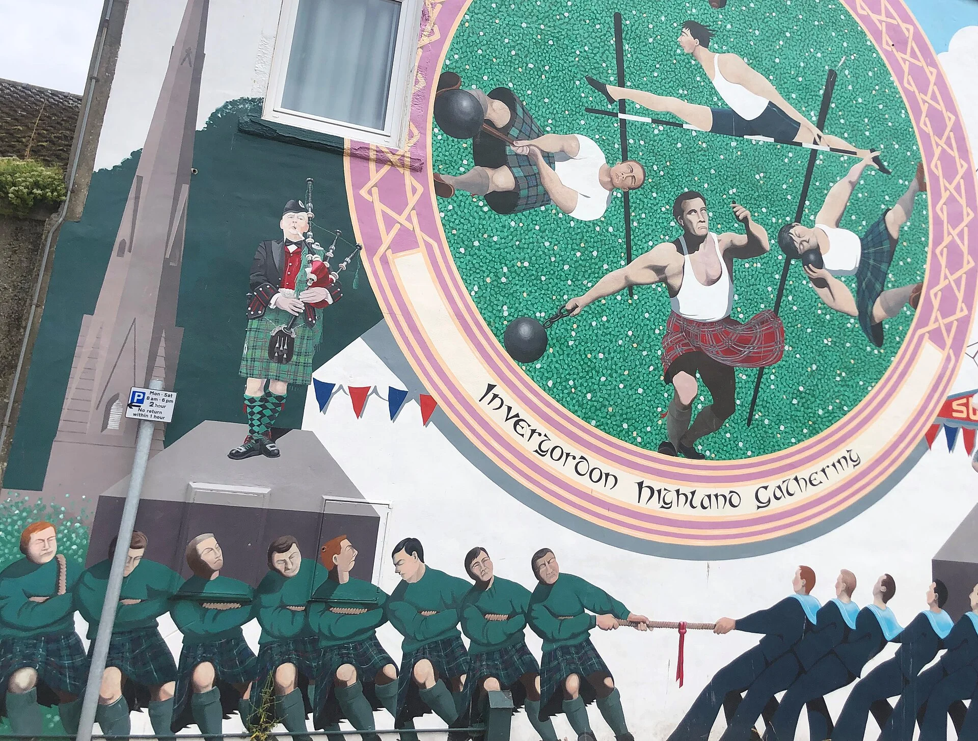 Wandgemälde „Invergordon Highland Gathering“ mit Dudelsackspieler, Highland-Games-Sportlern und Tauziehern an einer Hauswand in Invergordon.
