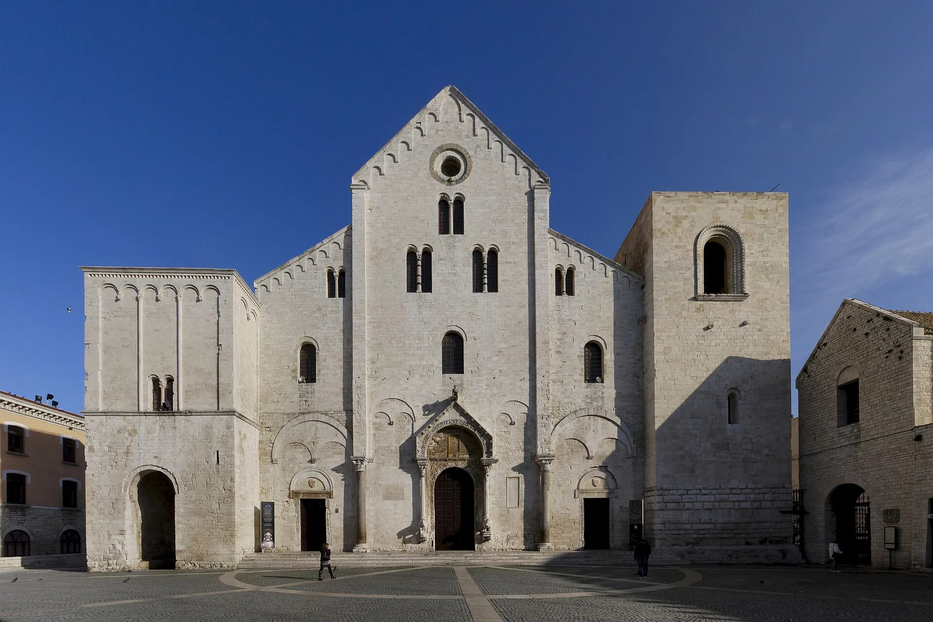 Die gesamte Westfassade der Basilica di San Nicola in Bari mit Vorplatz bei blauem Himmel.