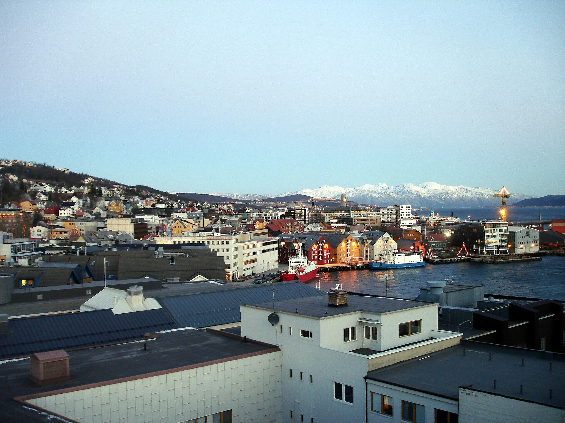 Erhöhter Blick über die Innenstadt von Tromsø auf die Hafenfront mit Kaianlagen und Booten am Prostneset.