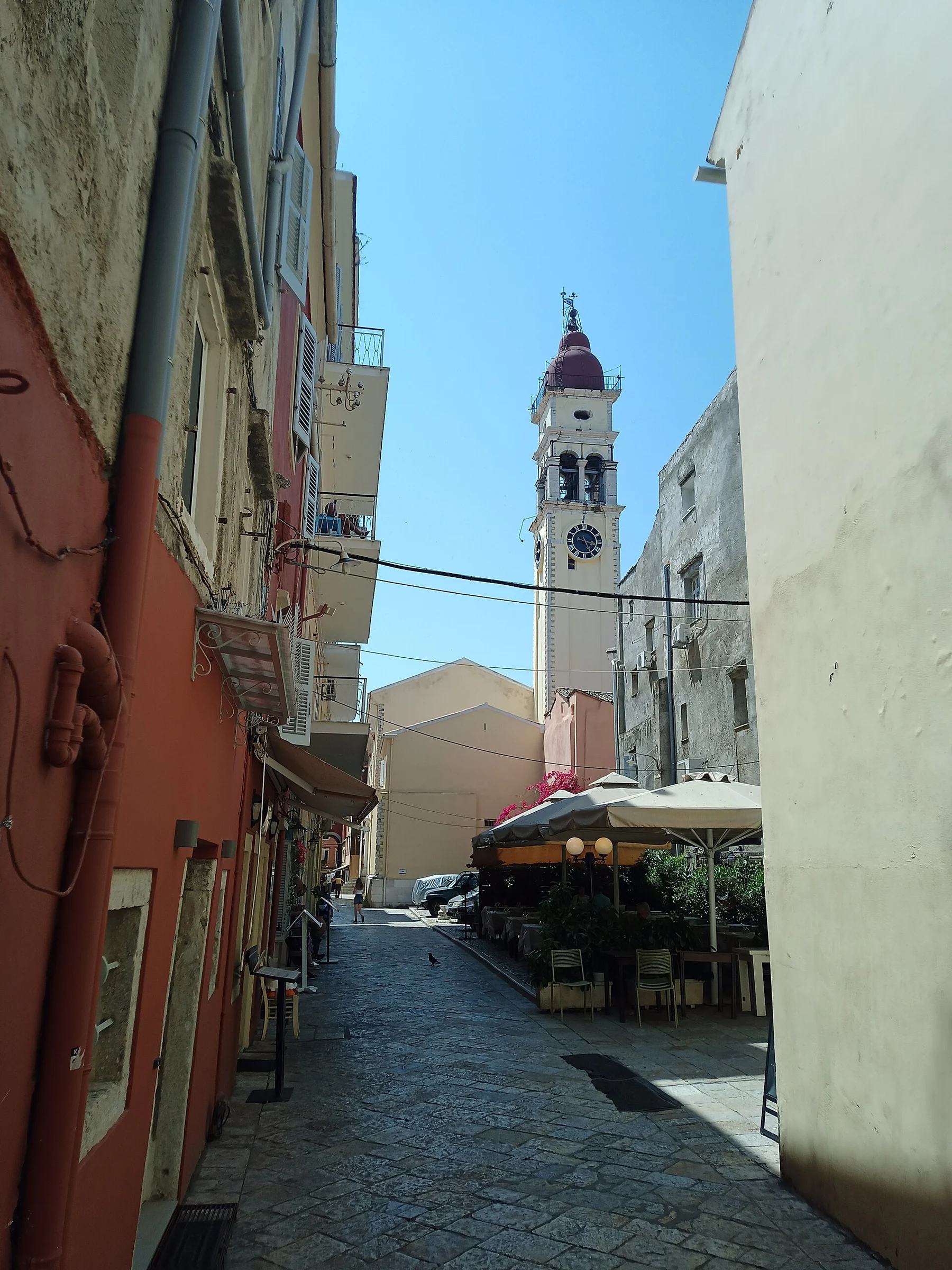 Blick durch eine Altstadtgasse von Kerkyra auf Korfu zum Glockenturm der Kirche Agios Spyridon mit rotem Kuppeldach.