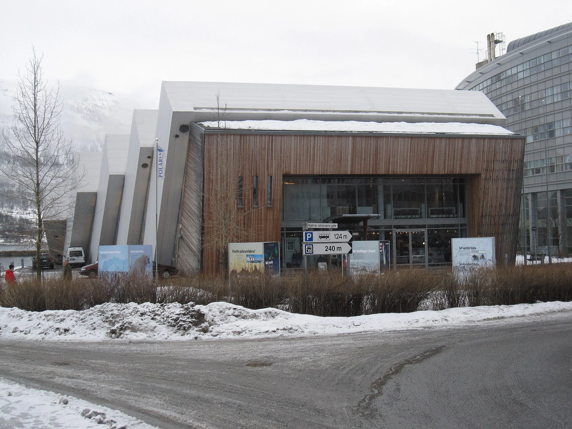 Eingangsseite von Polaria in Tromsø im Winter mit Holzfassade, Schriftzug und den schräg gestellten Plattenelementen.