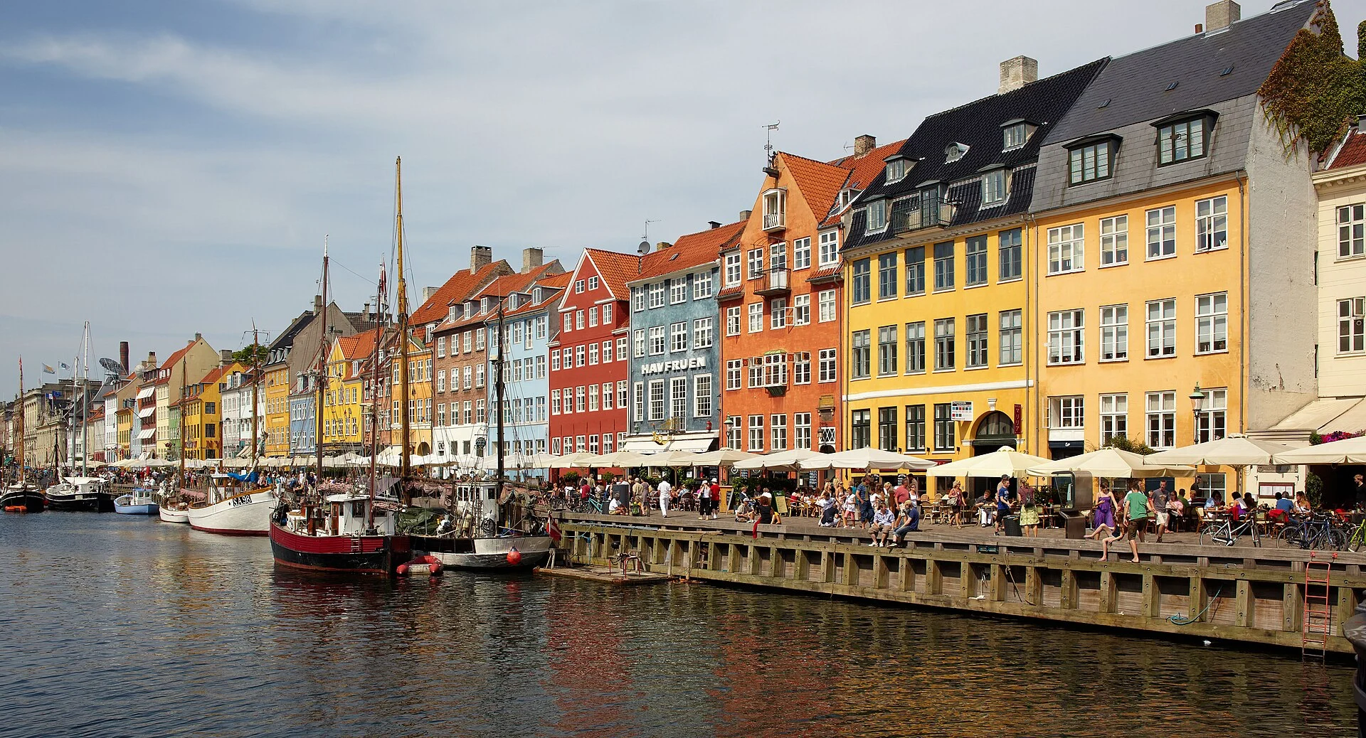 Der Kanal Nyhavn in Kopenhagen mit bunten Giebelhäusern, Holzbooten und belebter Kaipromenade.