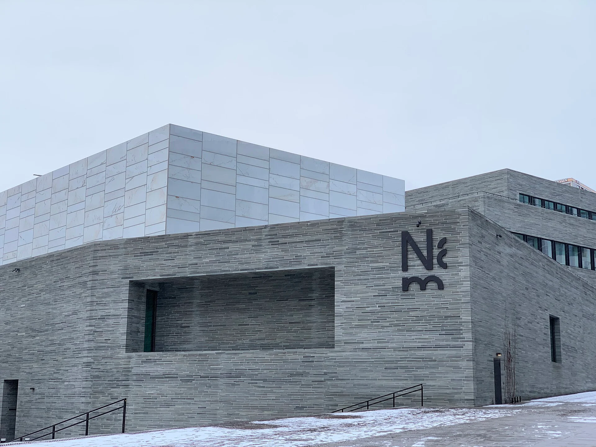 Das Nationalmuseum in Oslo im Winter mit Schieferfassade, NM-Logo und der hellen Lichthalle auf dem Dach.