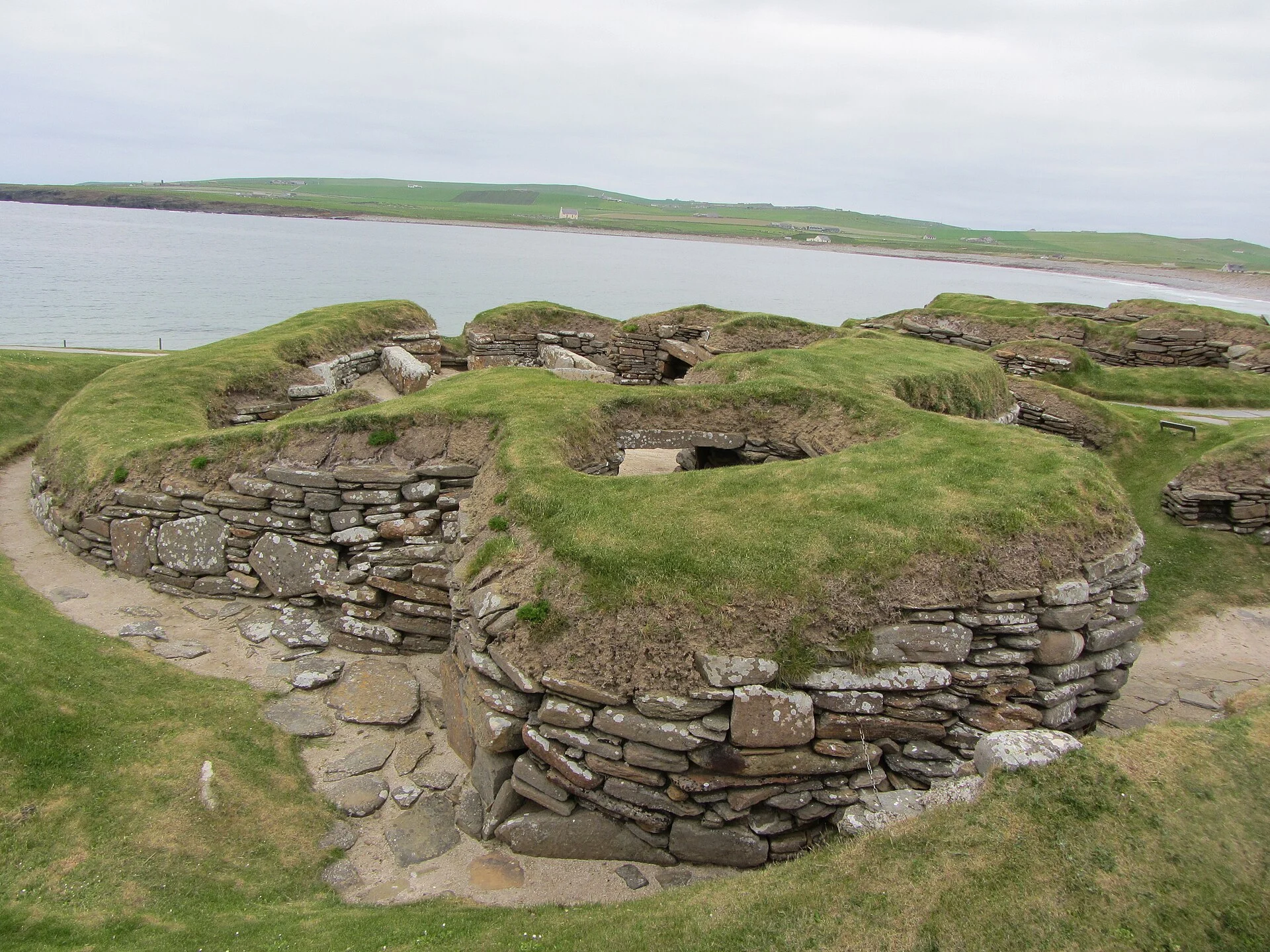 Rundliche Steinhäuser der jungsteinzeitlichen Siedlung Skara Brae mit Blick über die Bay of Skaill.