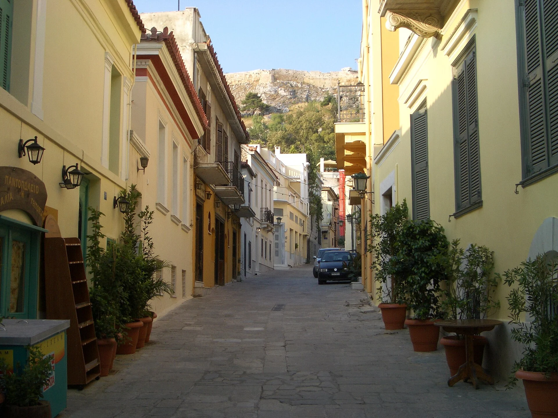 Gepflasterte Gasse mit bunten Häusern in Plaka, im Hintergrund der Felsen der Akropolis, Athen.