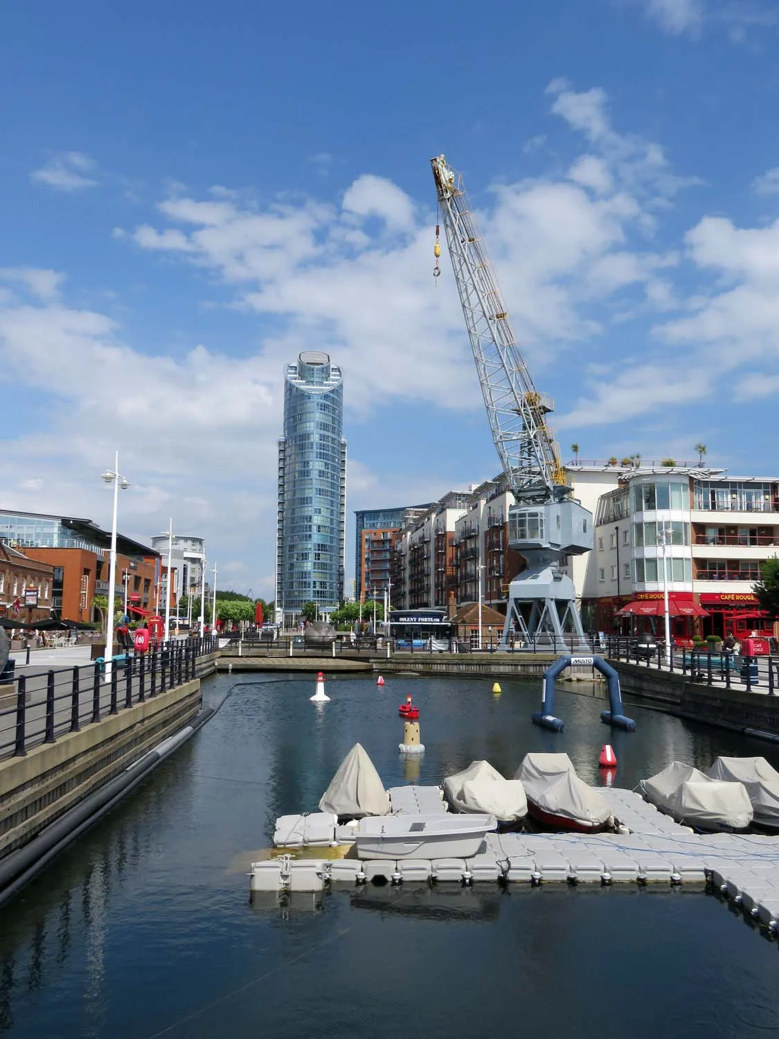 Das ehemalige Trockendock in Gunwharf Quays in Portsmouth mit historischem Hafenkran, Wohn- und Gastronomiegebäuden und dem Wohnturm No. 1 Gunwharf Quays im Hintergrund.