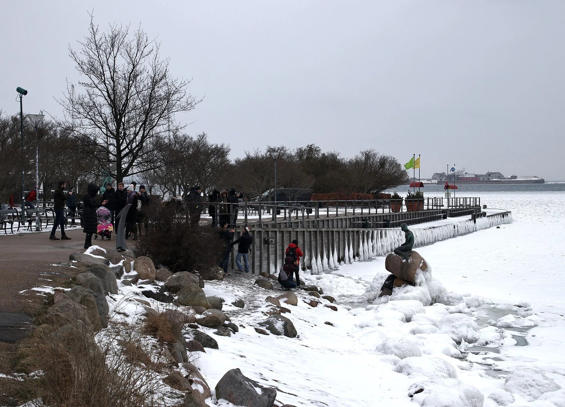 Winterliche Uferpromenade Langelinie in Kopenhagen mit der Kleinen Meerjungfrau auf ihrem vereisten Felsen und Besuchern.