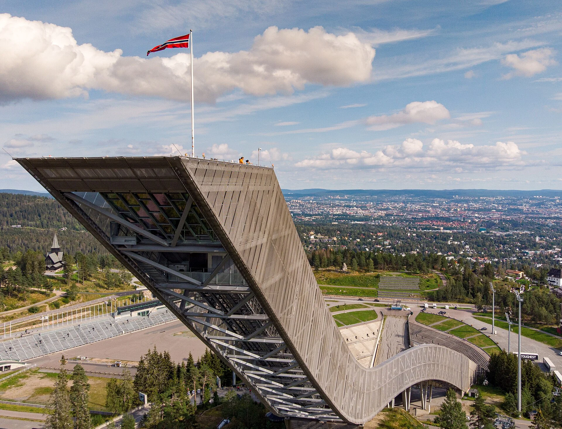 Die heutige Holmenkollbakken-Skisprungschanze in Oslo mit Aussichtsplattform und norwegischer Flagge, im Hintergrund die Stadt und der Oslofjord.