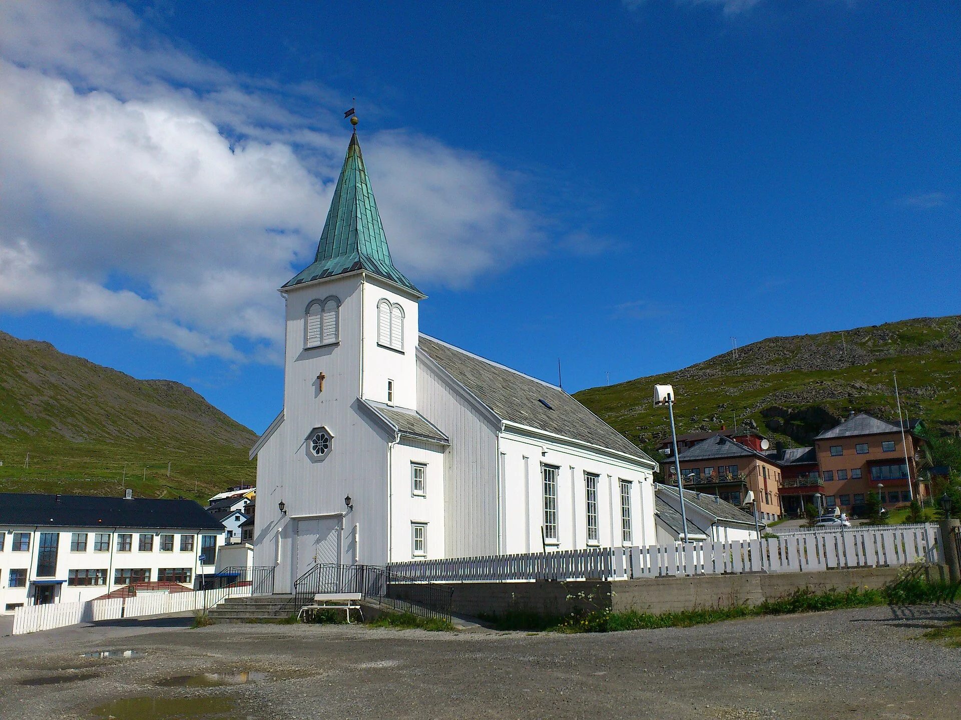 Die weiße Holzkirche von Honningsvåg von 1885 mit grünem Turmhelm bei blauem Himmel.