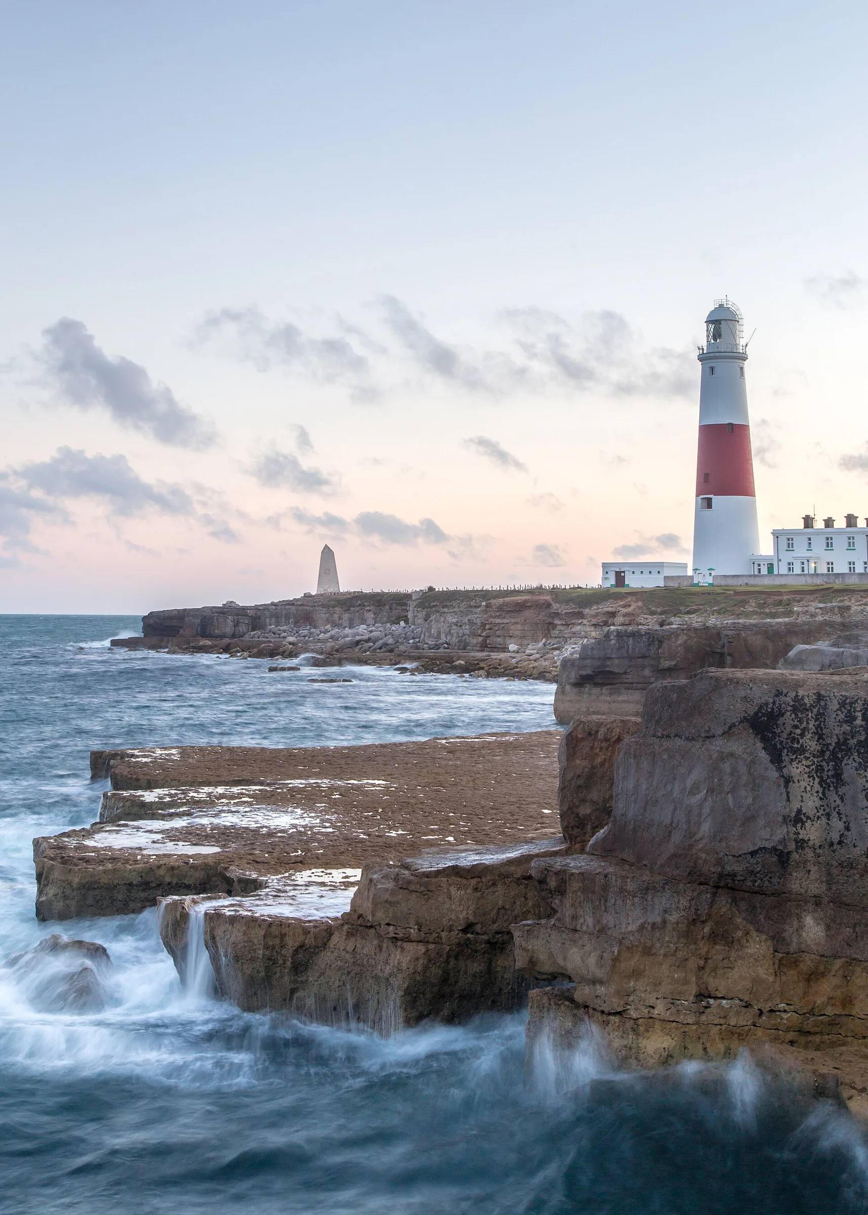 Portland Bill Lighthouse und Trinity-House-Obelisk über den Felsplatten der Isle of Portland bei Sonnenuntergang mit Brandung.