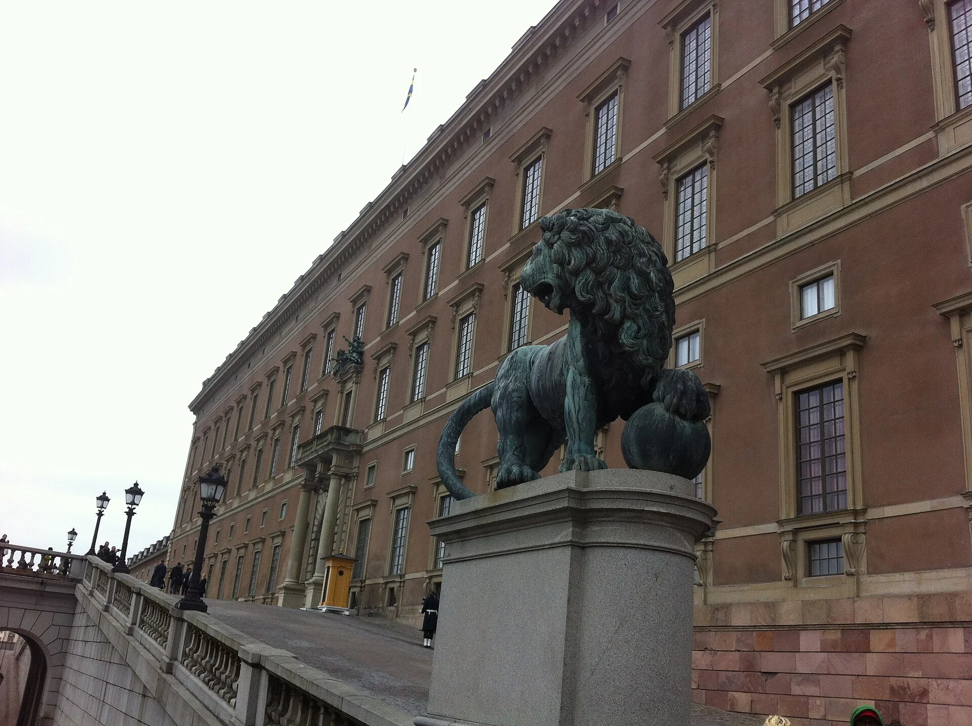 Fassade des Königlichen Schlosses in Stockholm mit dem bronzenen Löwen auf der Terrasse und schwedischer Flagge.