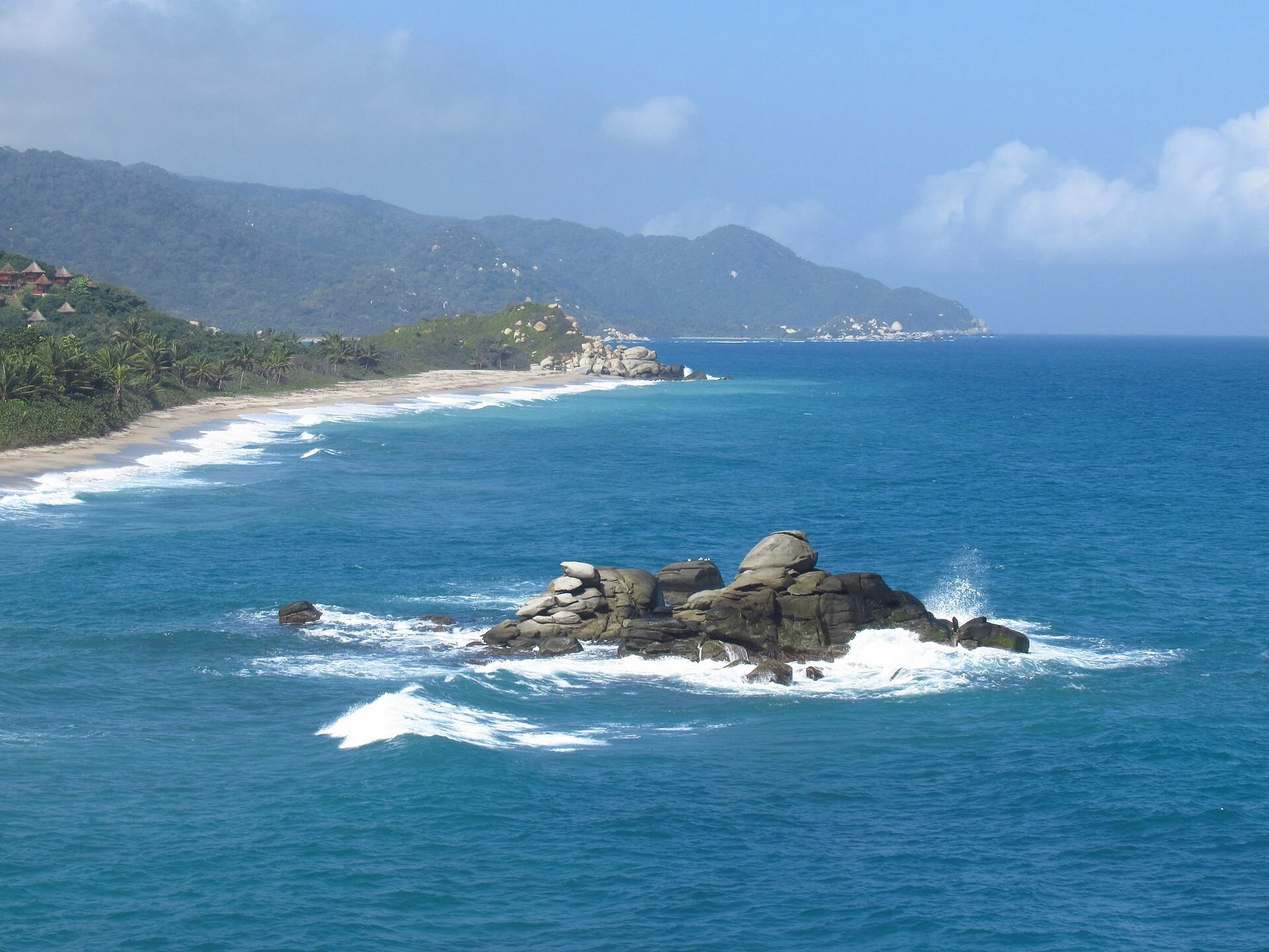 Die Küste des Tayrona-Nationalparks mit Felsen in der Brandung und Regenwald dahinter