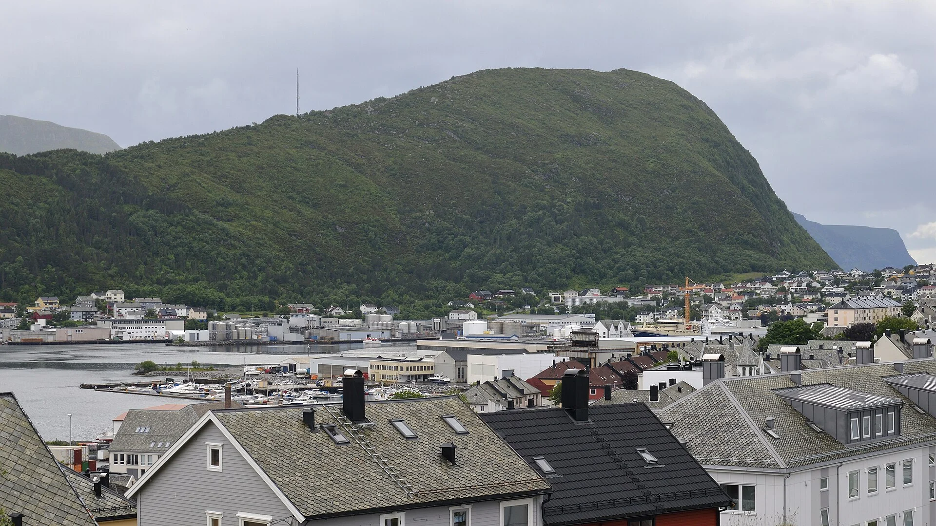 Der Berg Sukkertoppen auf der Insel Hessa über dem Hafen von Ålesund, gesehen über die Dächer der Stadt