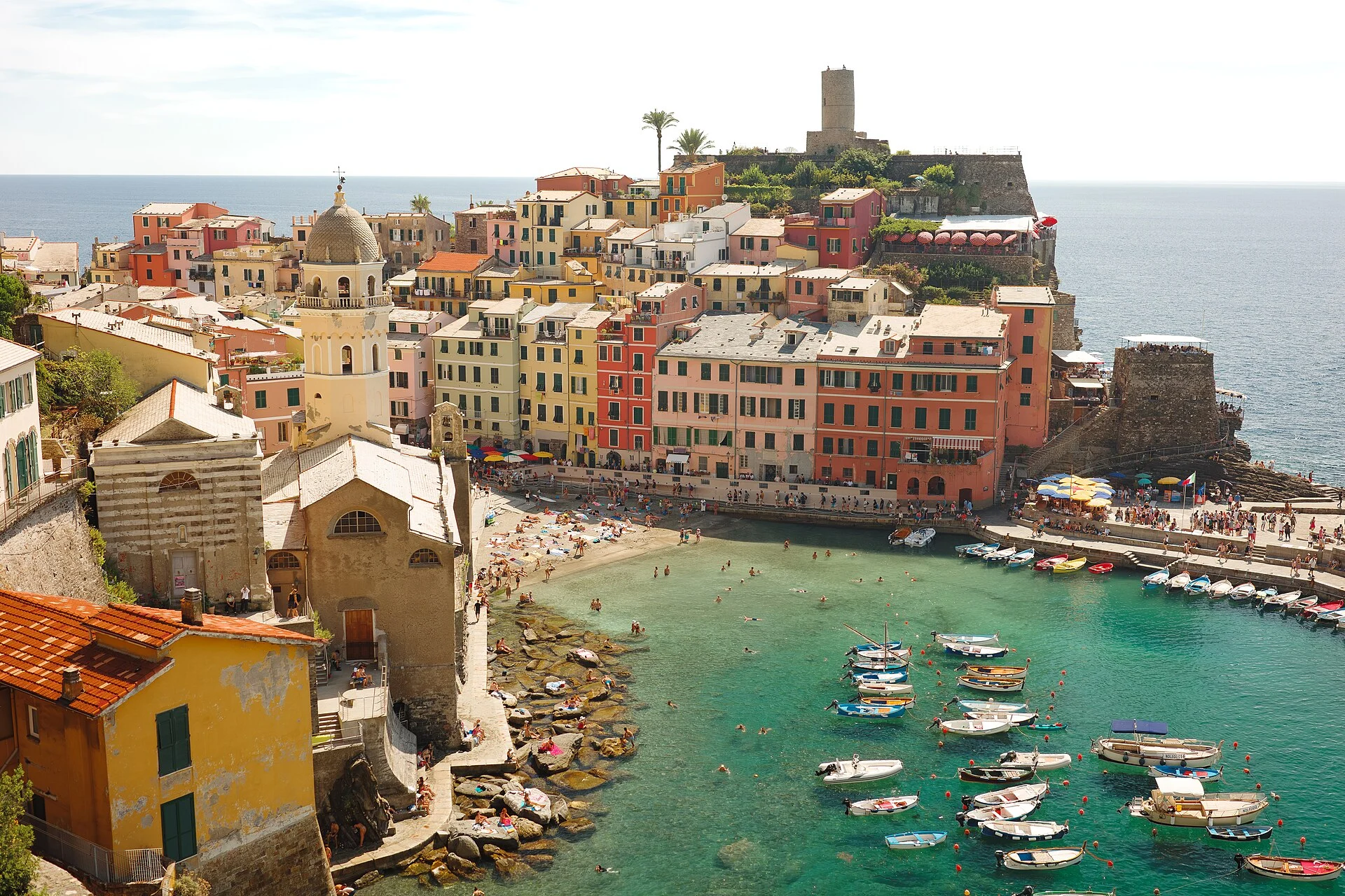 Naturhafen von Vernazza mit Booten, Strand, Kirche Santa Margherita di Antiochia und farbigen Häusern.