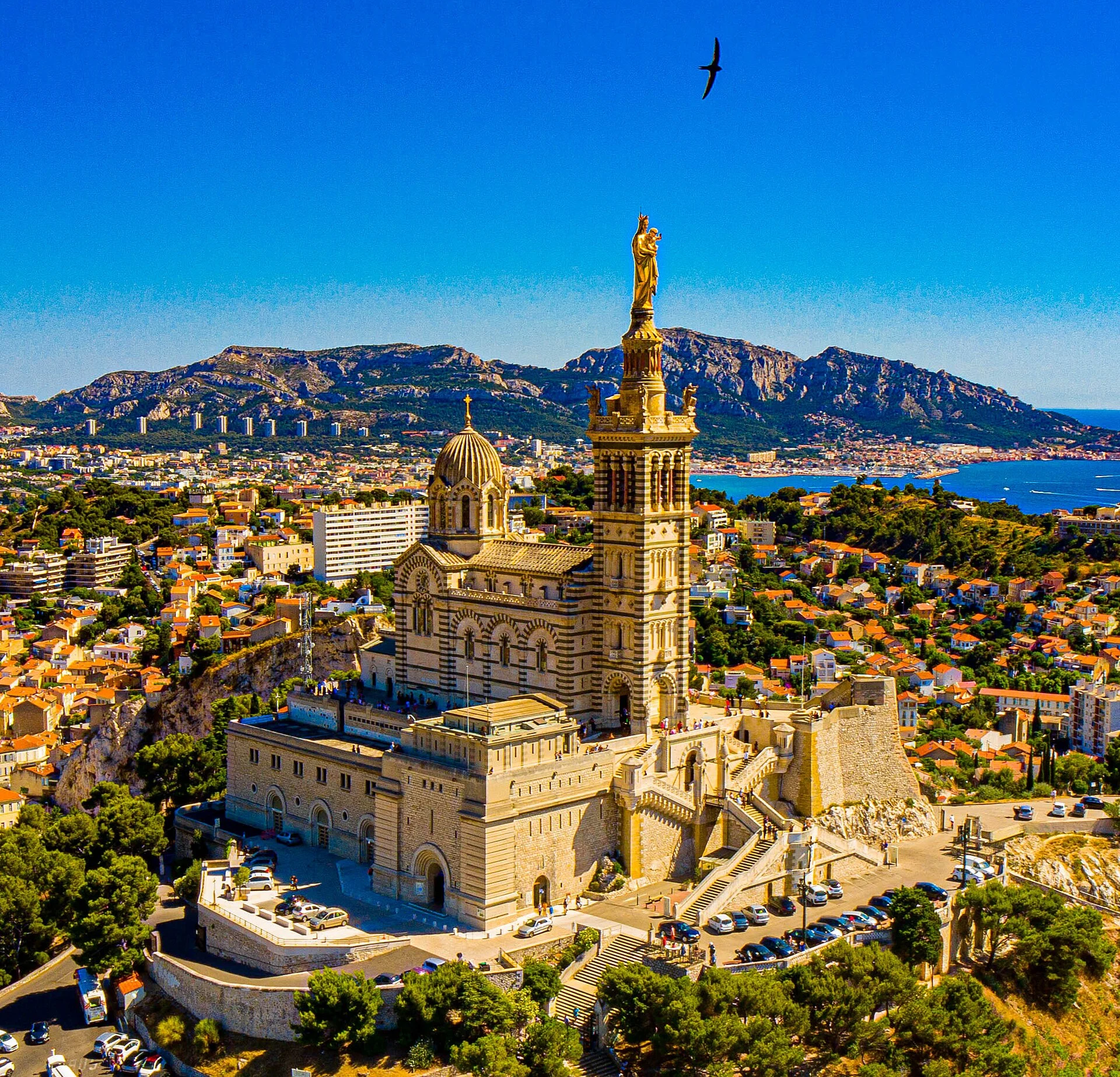 Luftaufnahme der Basilika Notre-Dame de la Garde in Marseille mit vergoldeter Marienstatue auf dem Glockenturm.