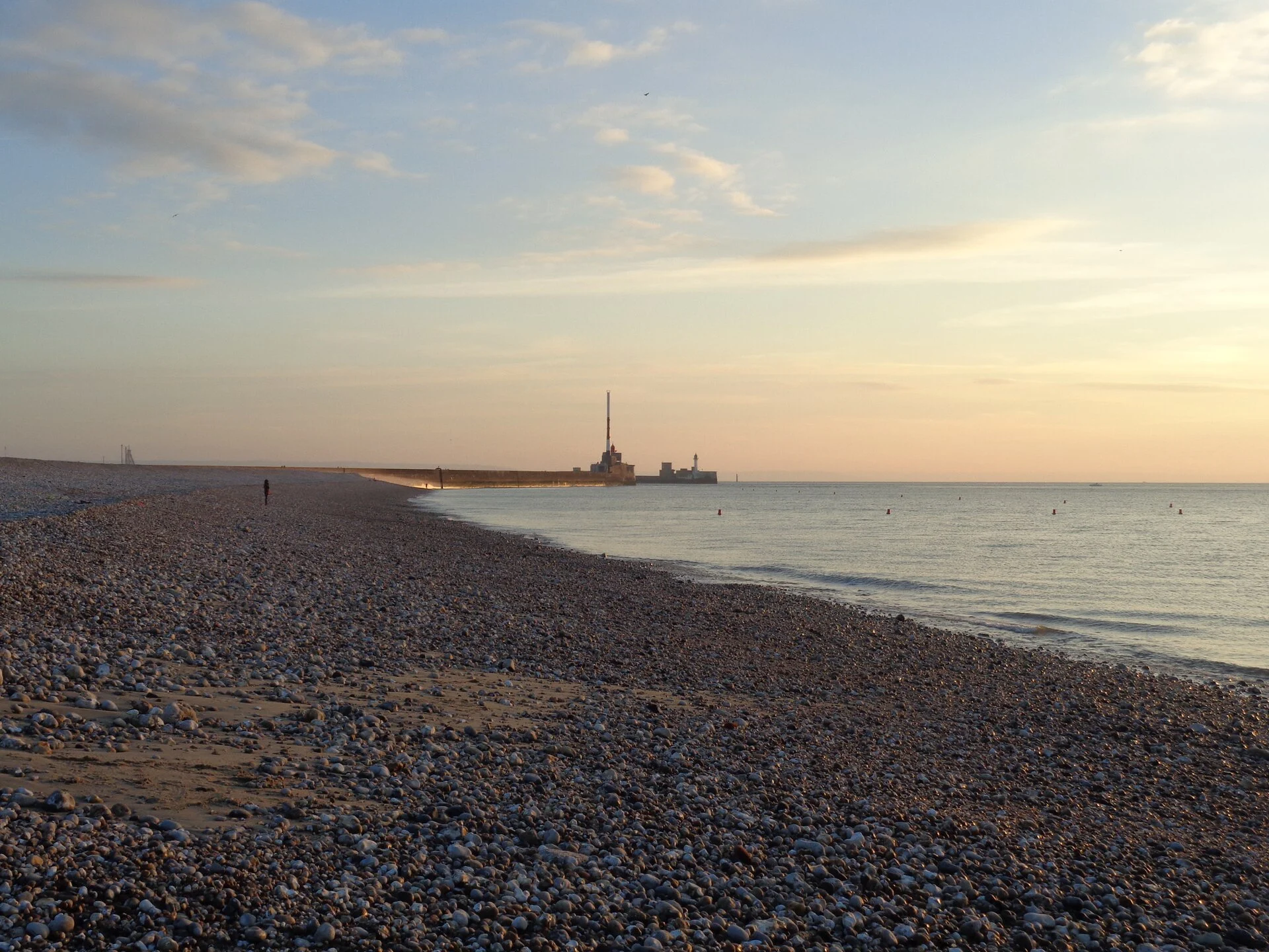 Kiesstrand von Le Havre im Abendlicht mit Blick auf die Hafeneinfahrt und den Leuchtturm der Mole.