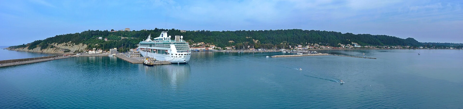 Der Hafen von Katakolon mit einem Kreuzfahrtschiff am Kai und dem bewaldeten Ufer dahinter