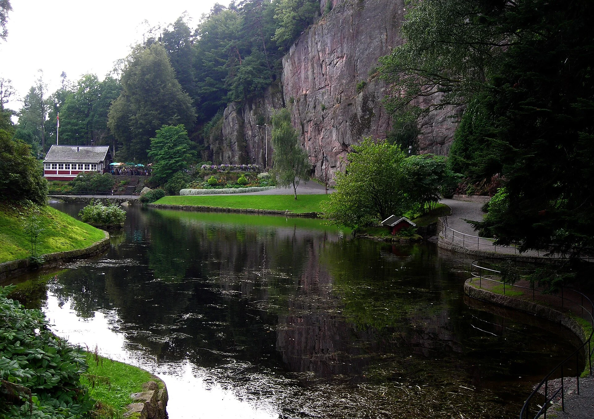 Teich im Ravnedalen naturpark in Kristiansand mit Restaurantgebäude und steiler Felswand im Hintergrund.