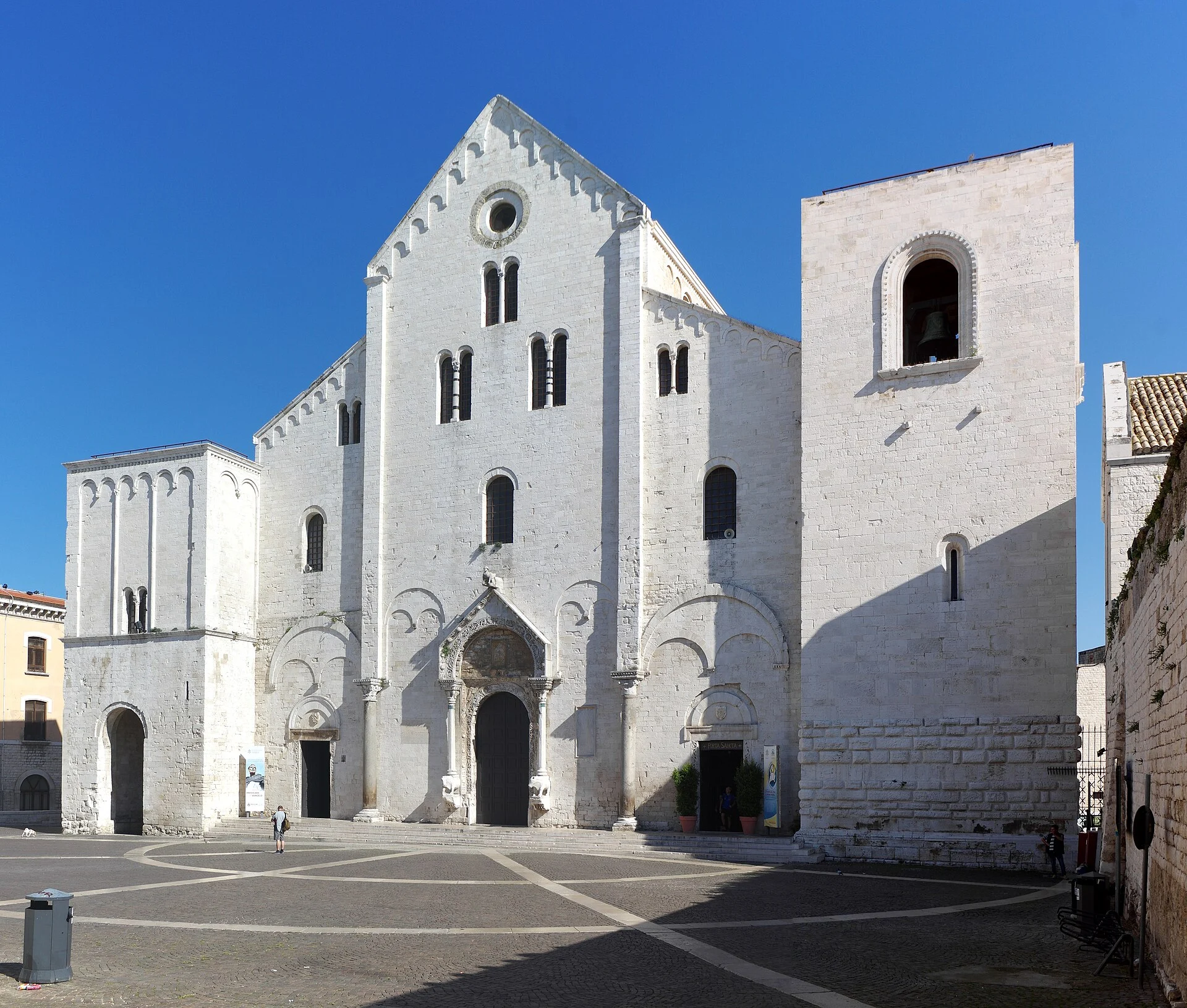 Die weiße romanische Fassade der Basilika San Nicola in der Altstadt von Bari mit Glockenturm und leerem Vorplatz.