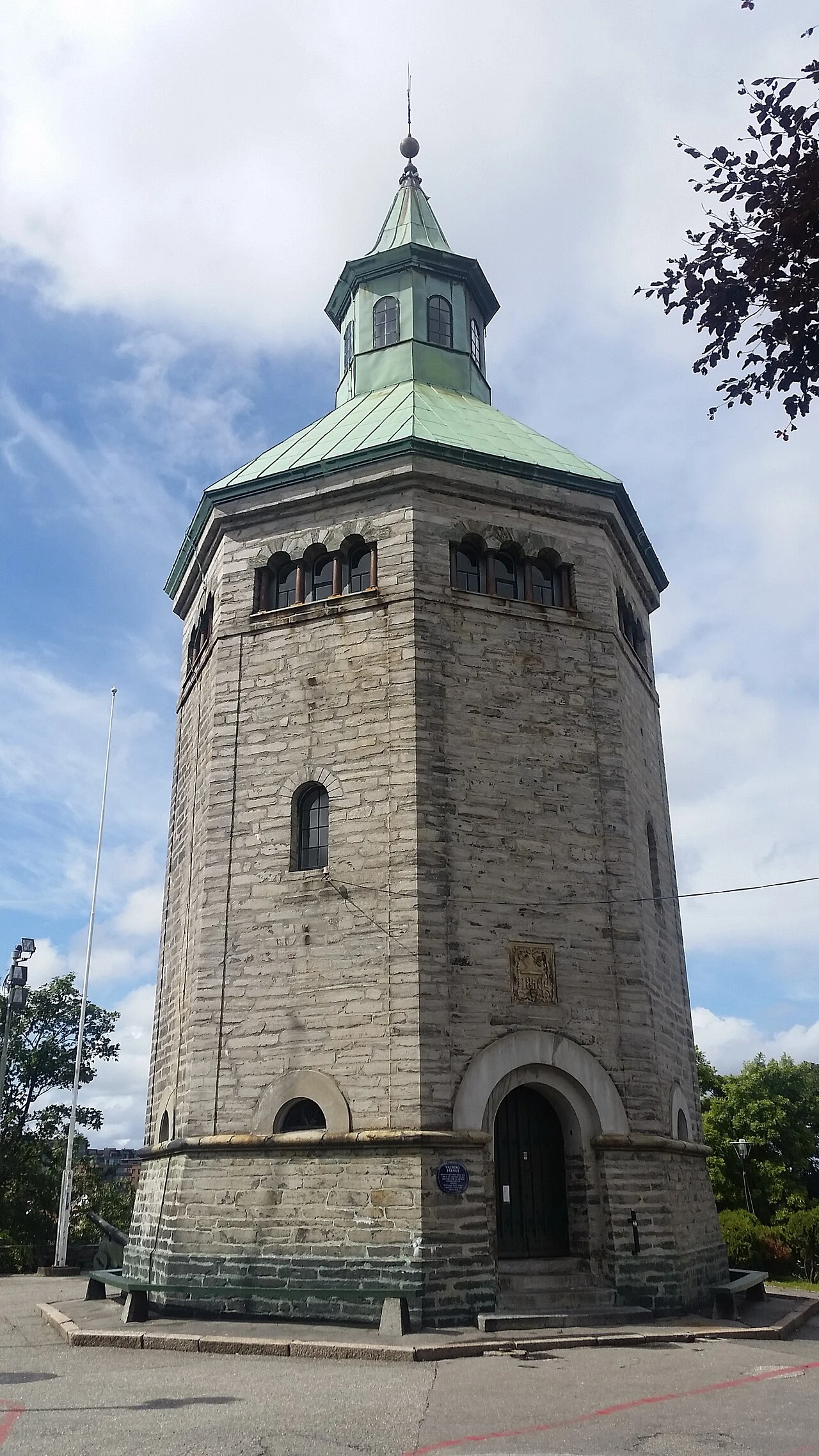 Das Valbergtårnet in Stavanger, ein achteckiger Steinturm mit grünem Kupferdach, mit Eingang und Vorplatz bei Sonnenschein.