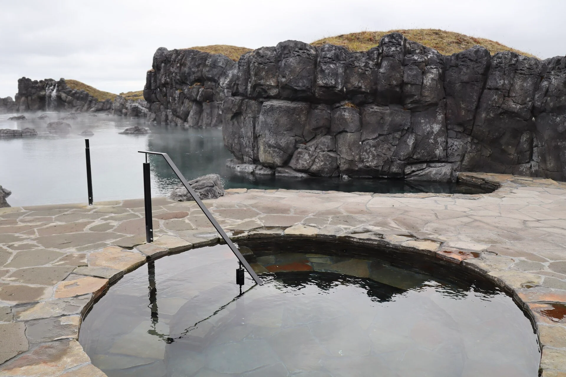 Ein Becken der Sky Lagoon am Meer, mit Dampf über dem Wasser