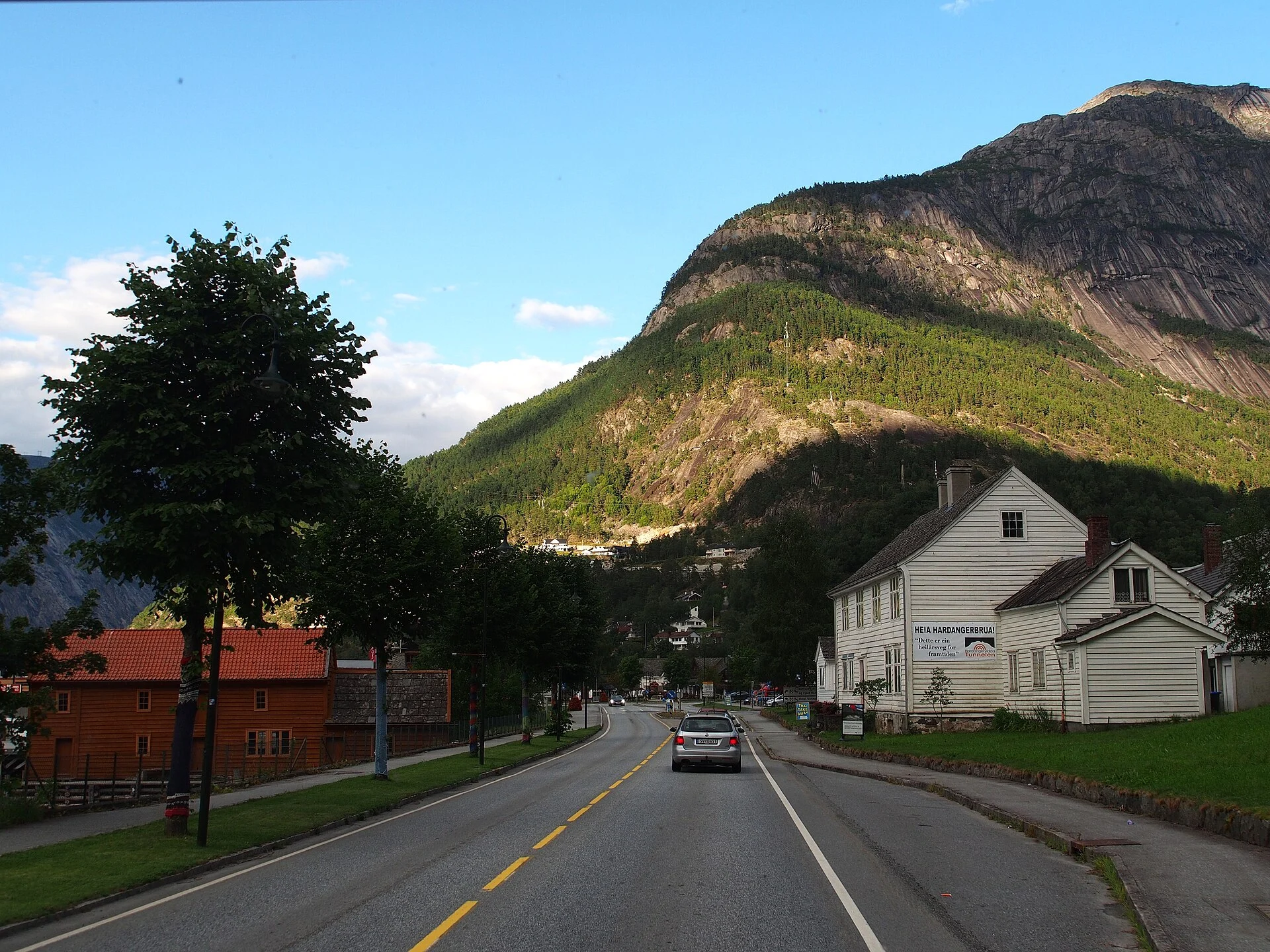 Ortsdurchfahrt von Eidfjord mit weißem Holzhaus und Bergkulisse, Norwegen.