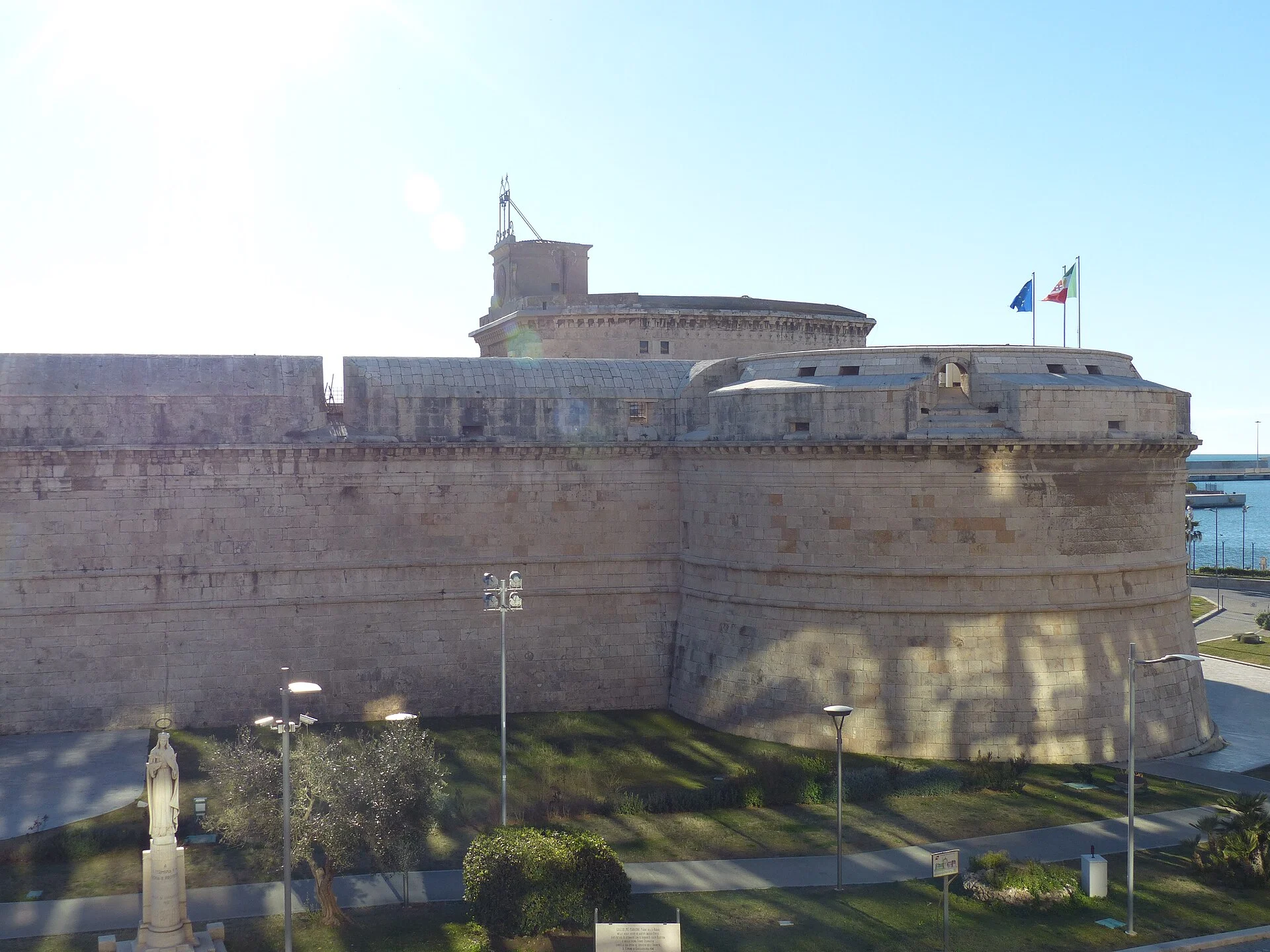 Mauern und Rundbastion des Forte Michelangelo in Civitavecchia bei Sonnenschein, dahinter der Maschio-Turm und das Meer.