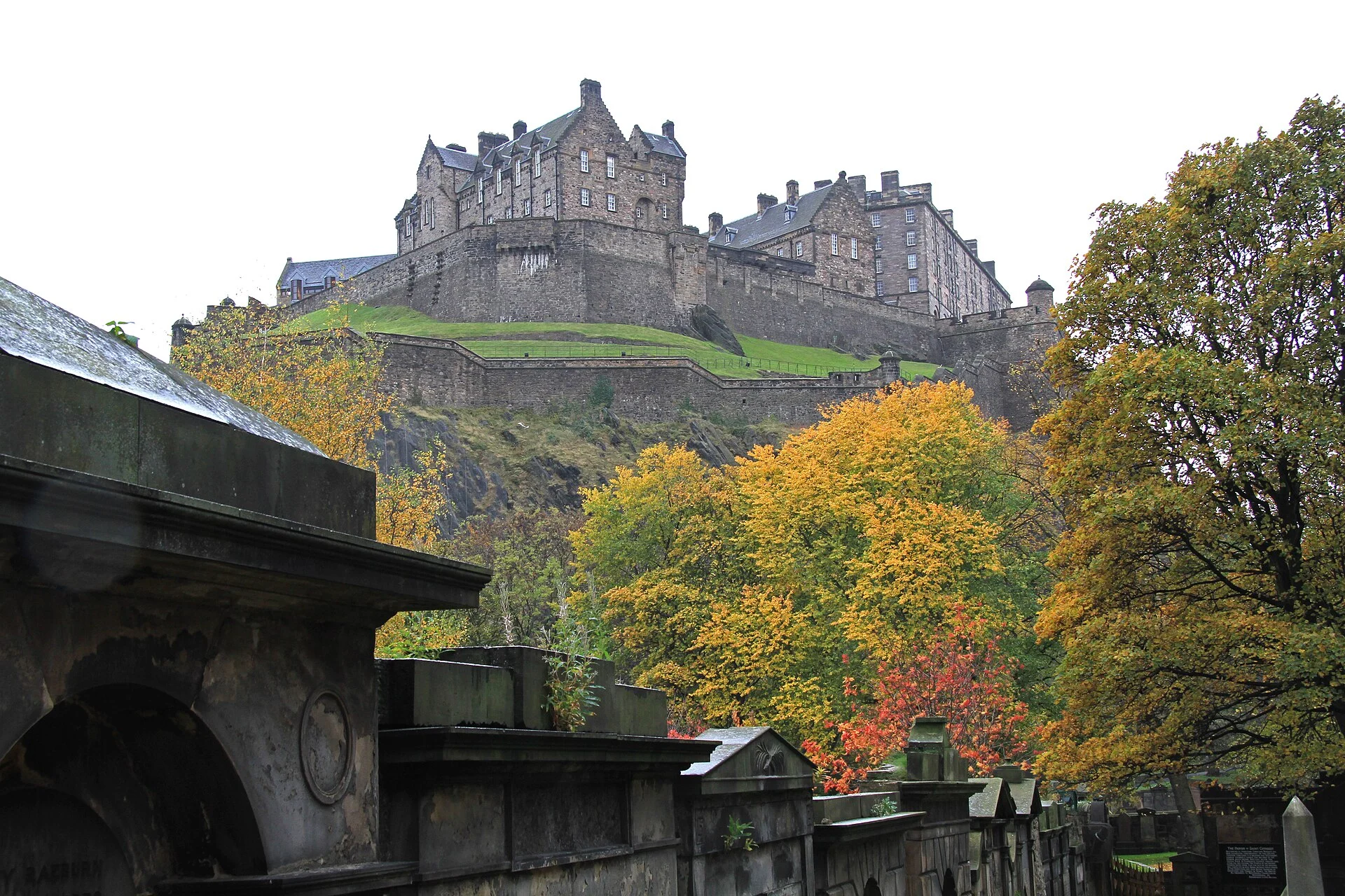 Edinburgh Castle auf dem Vulkanfelsen, gesehen vom Friedhof St. Cuthbert's mit herbstlichen Bäumen.