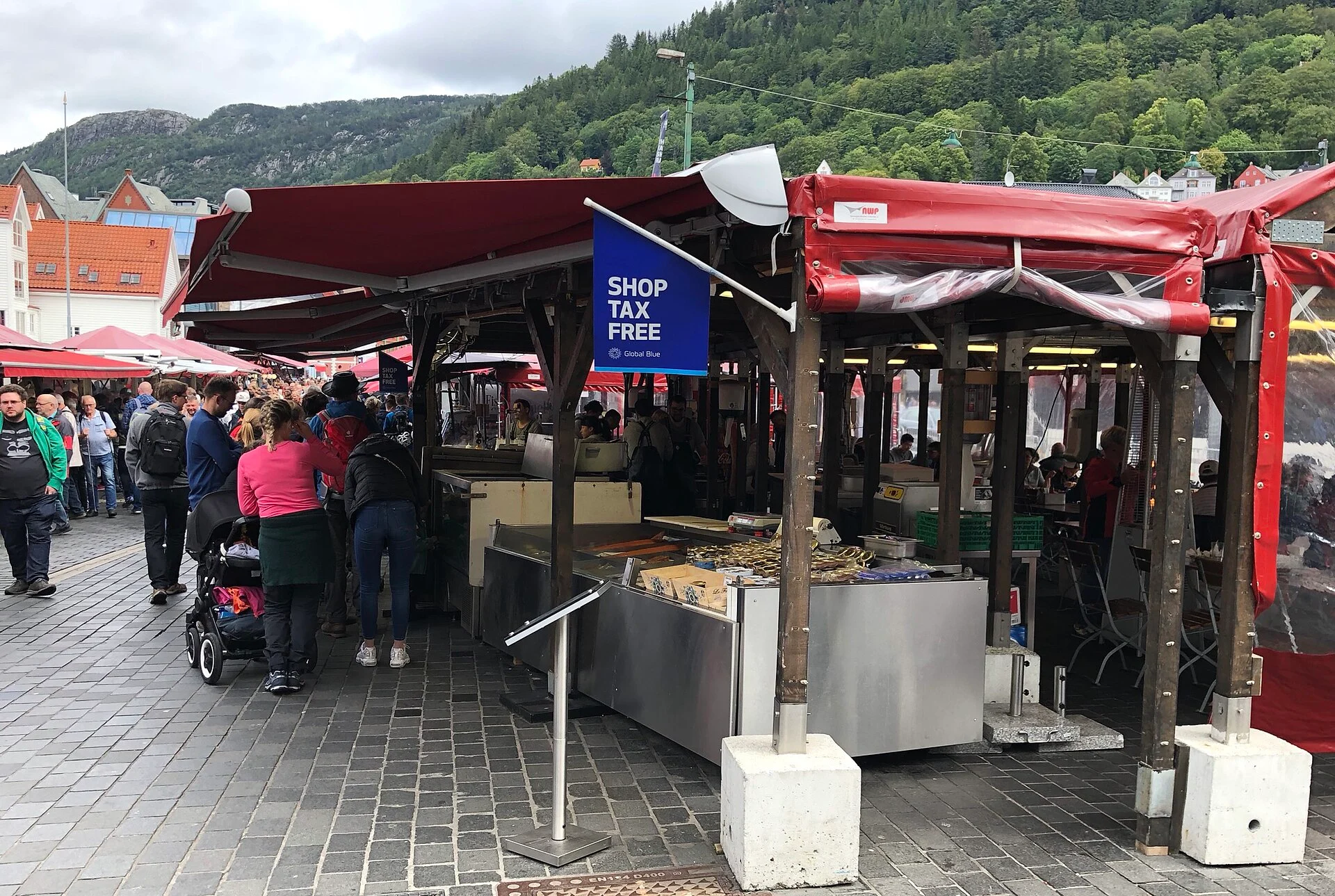Marktstände mit roten Dächern am Fisketorget in Bergen, im Hintergrund bewaldete Hänge und Stadthäuser.