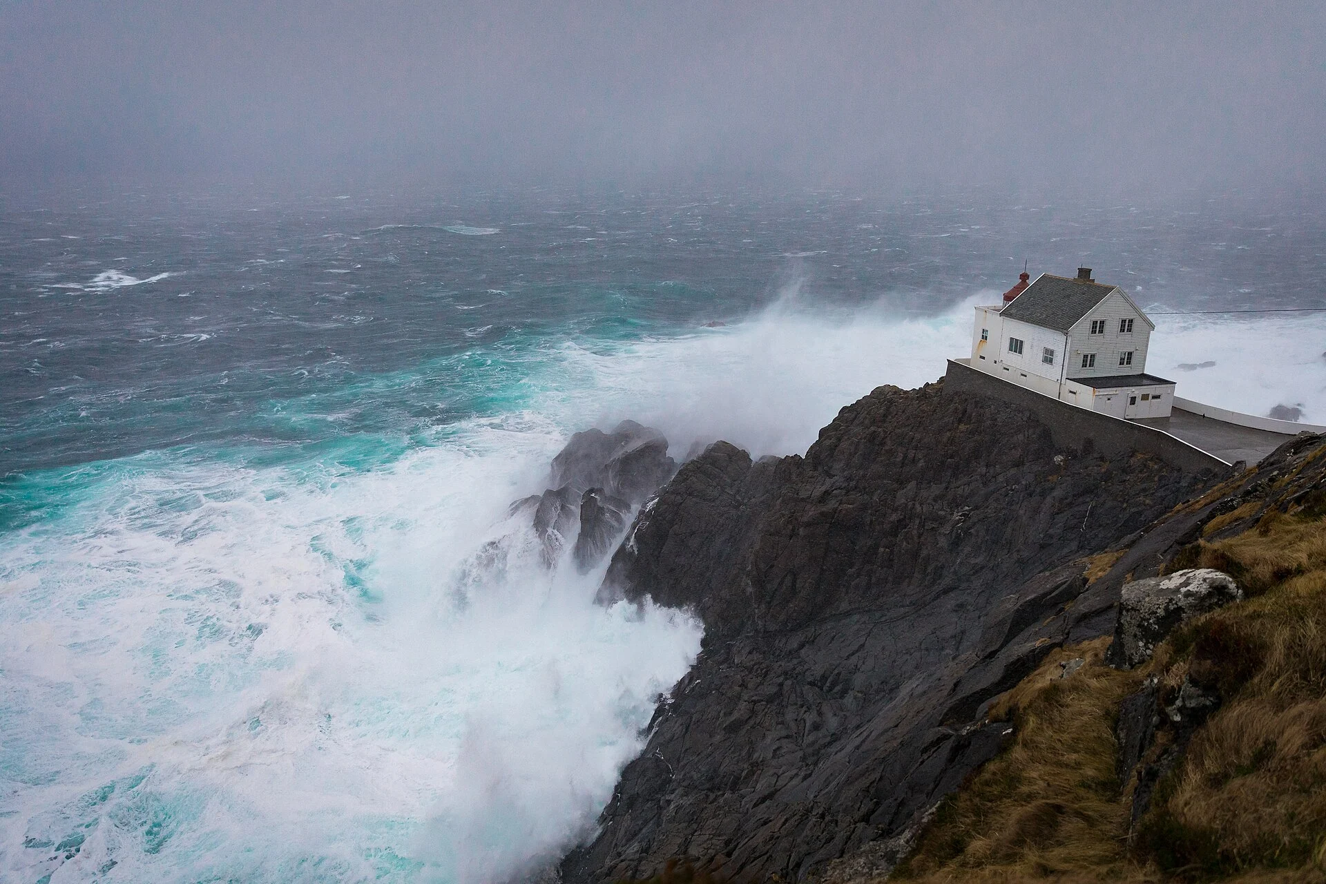 Der Leuchtturm Kråkenes auf der Klippe, davor hochschlagende Brandung