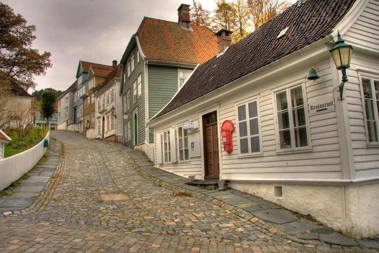 Kopfsteingepflasterte Gasse mit historischen Holzhäusern im Freilichtmuseum Gamle Bergen.