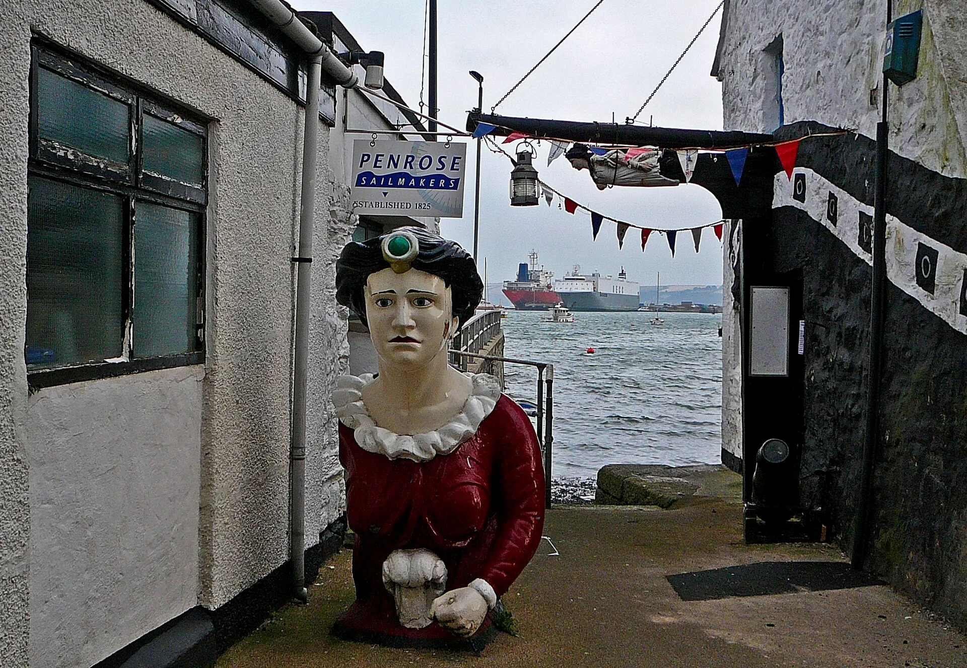 Der schmale Durchgang Upton Slip in Falmouth führt zwischen Häusern hinunter zum Wasser, mit Schild der Segelmacherei Penrose und einer Galionsfigur.