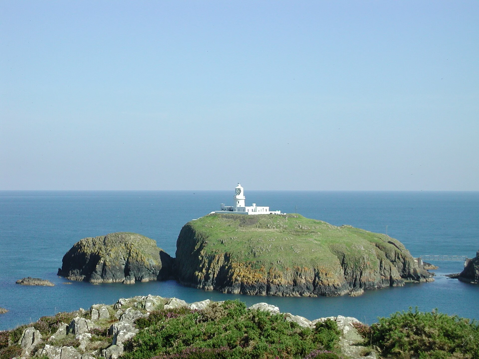 Strumble Head Lighthouse auf der kleinen Insel Ynys Meicel mit Fußgängerbrücke zum Festland bei Fishguard, Wales.