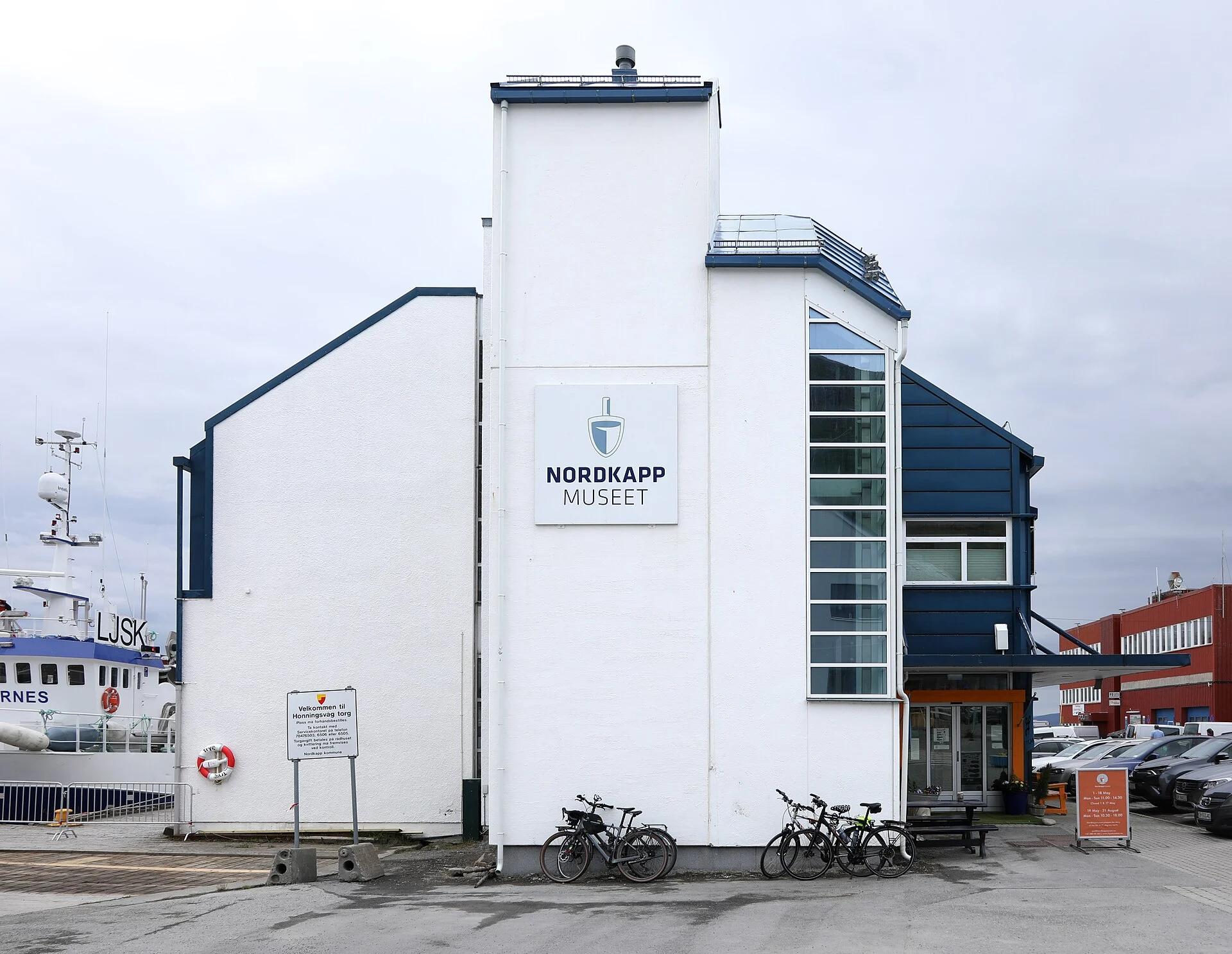 Weiß-blaues Gebäude des Nordkappmuseet mit großem Logo-Schild am Hafen von Honningsvåg, daneben ein Fischereischiff.