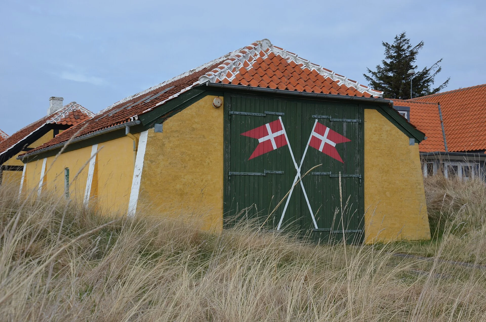 Gelb gestrichenes Haus mit rotem Ziegeldach und dänischen Flaggen in den Dünen bei Skagen
