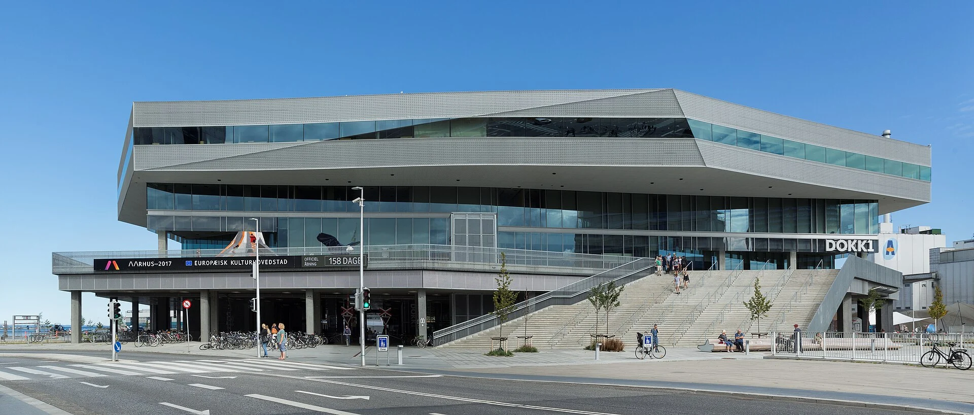 Das Bibliotheks- und Kulturzentrum Dokk1 in Aarhus mit auskragender Metallfassade, Freitreppe und Schriftzug DOKK1, gesehen vom Europa Plads.