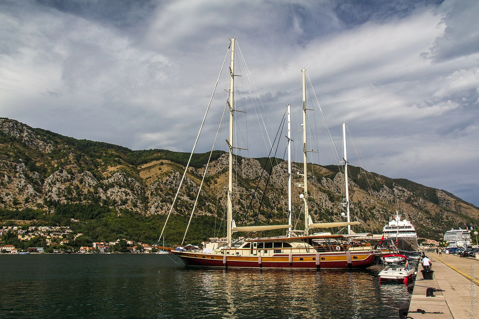 Segelyacht und Kreuzfahrtschiff am Kai von Kotor vor der steilen Bergkulisse der Bucht, Montenegro.
