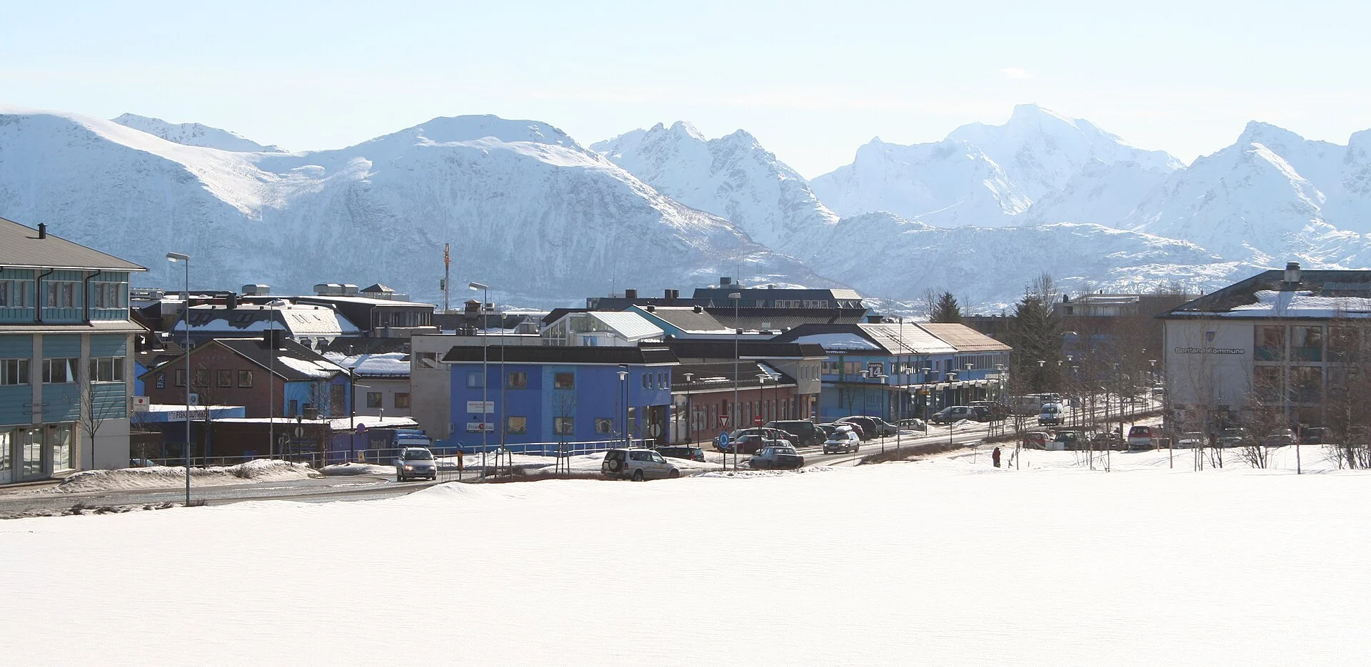 Blau gestrichene Gebäude im Ortszentrum von Sortland (Blåbyen) vor schneebedeckten Bergen der Vesterålen.