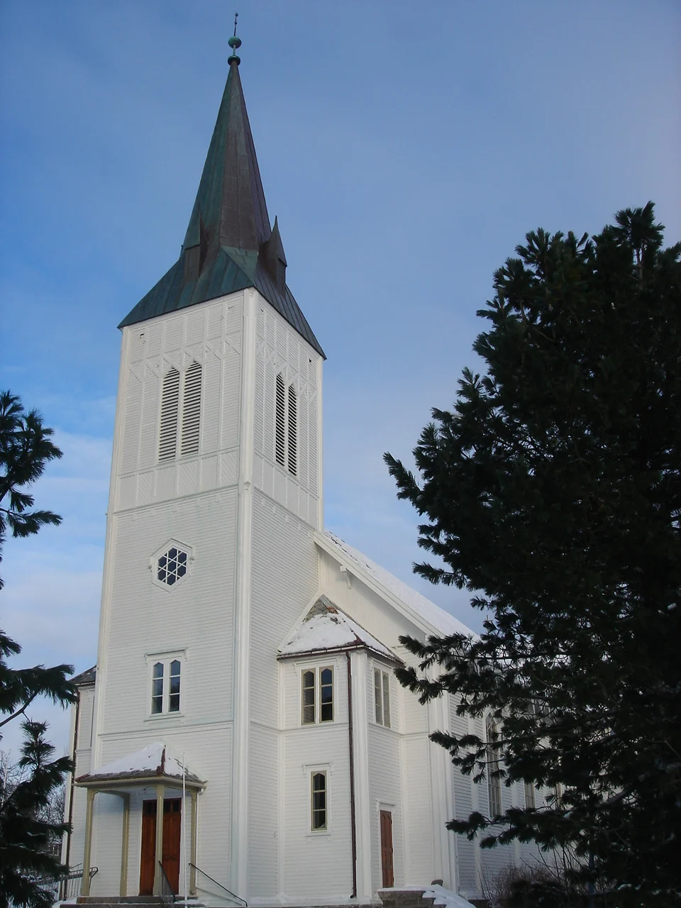 Die weiße Holzkirche Sortland kirke in Sortland, Norwegen, mit hohem Turm und grün patinierter Spitze bei Winterlicht.