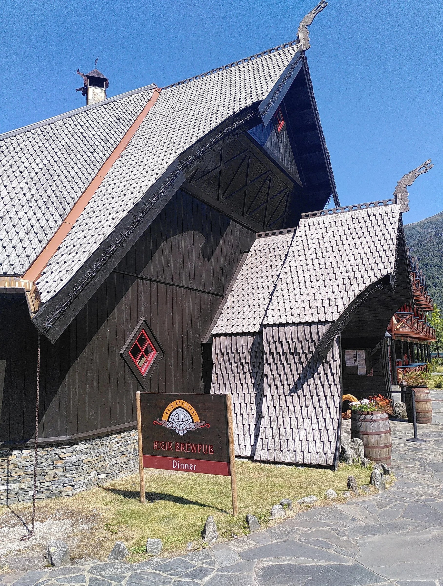 Das dunkle Holzgebäude des Ægir BrewPub in Flåm mit Schindeldach, Drachenköpfen und Schild „Ægir Brewpub – Dinner“.