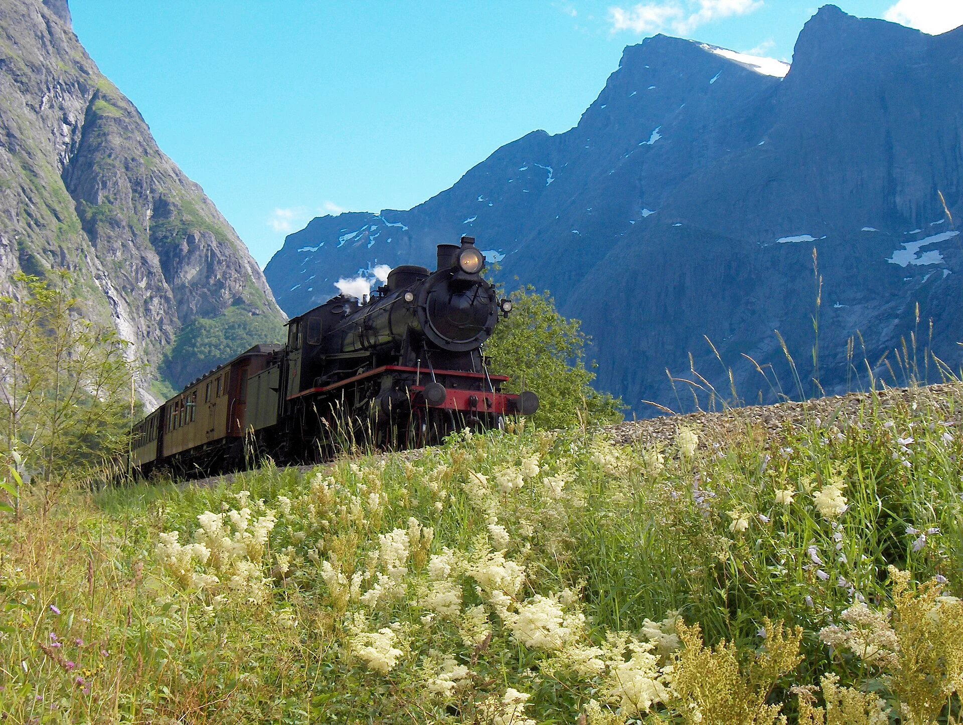 Ein Dampfzug der Raumabahn im Romsdal vor den Steilwänden des Tals