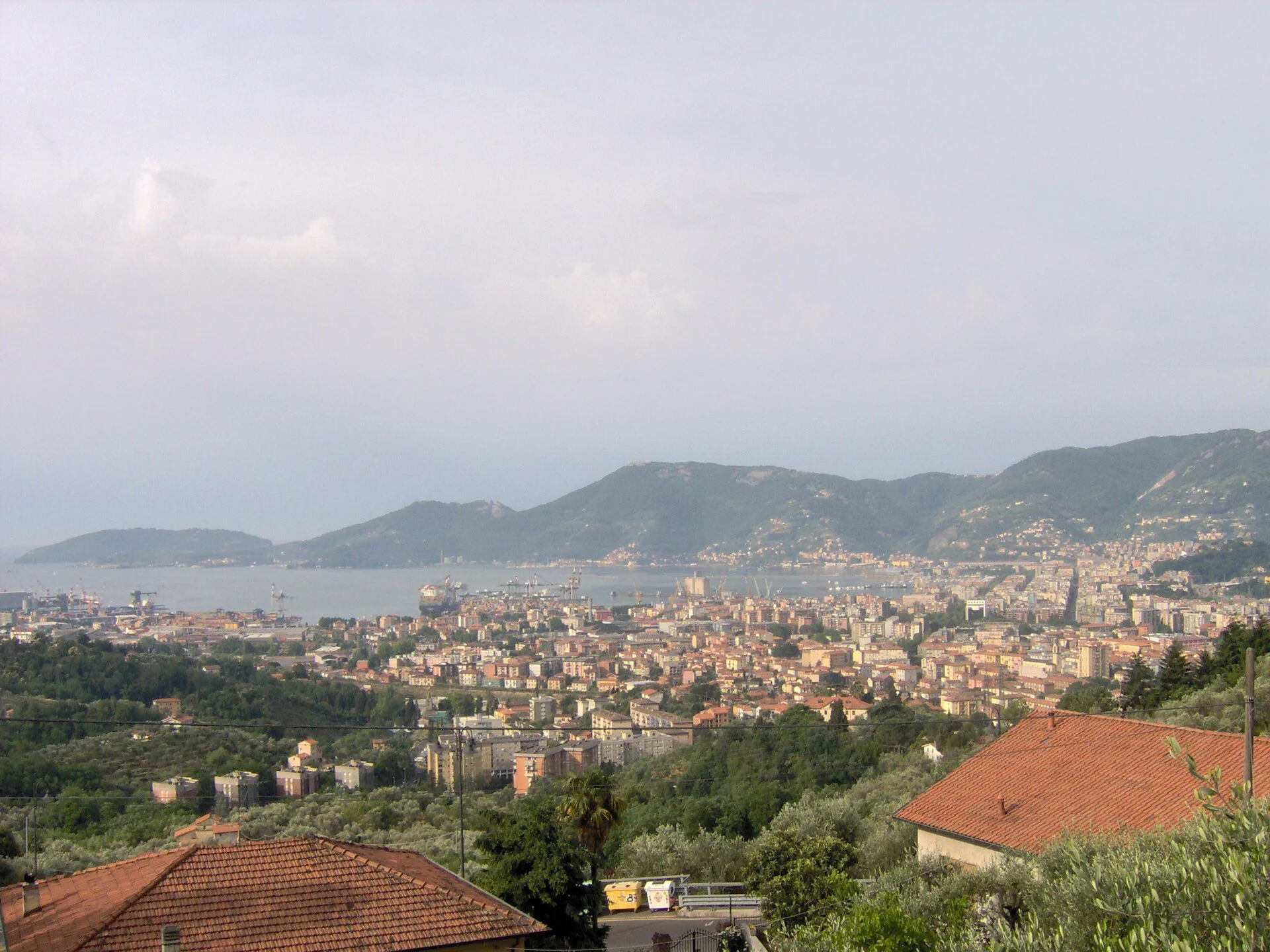 Blick von den Hügeln bei Carozzo auf La Spezia, Italien, mit Golf, Hafenanlagen und bewaldeten Bergen.