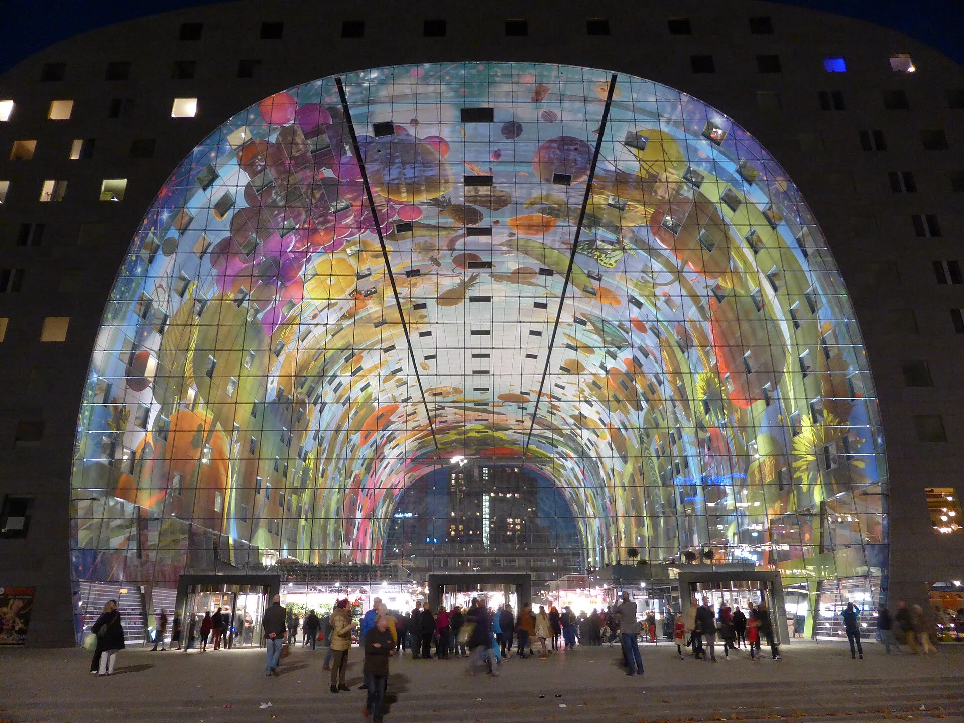 Die Markthal in Rotterdam bei Abenddämmerung mit beleuchtetem Glasbogen und dem farbigen Deckengemälde.