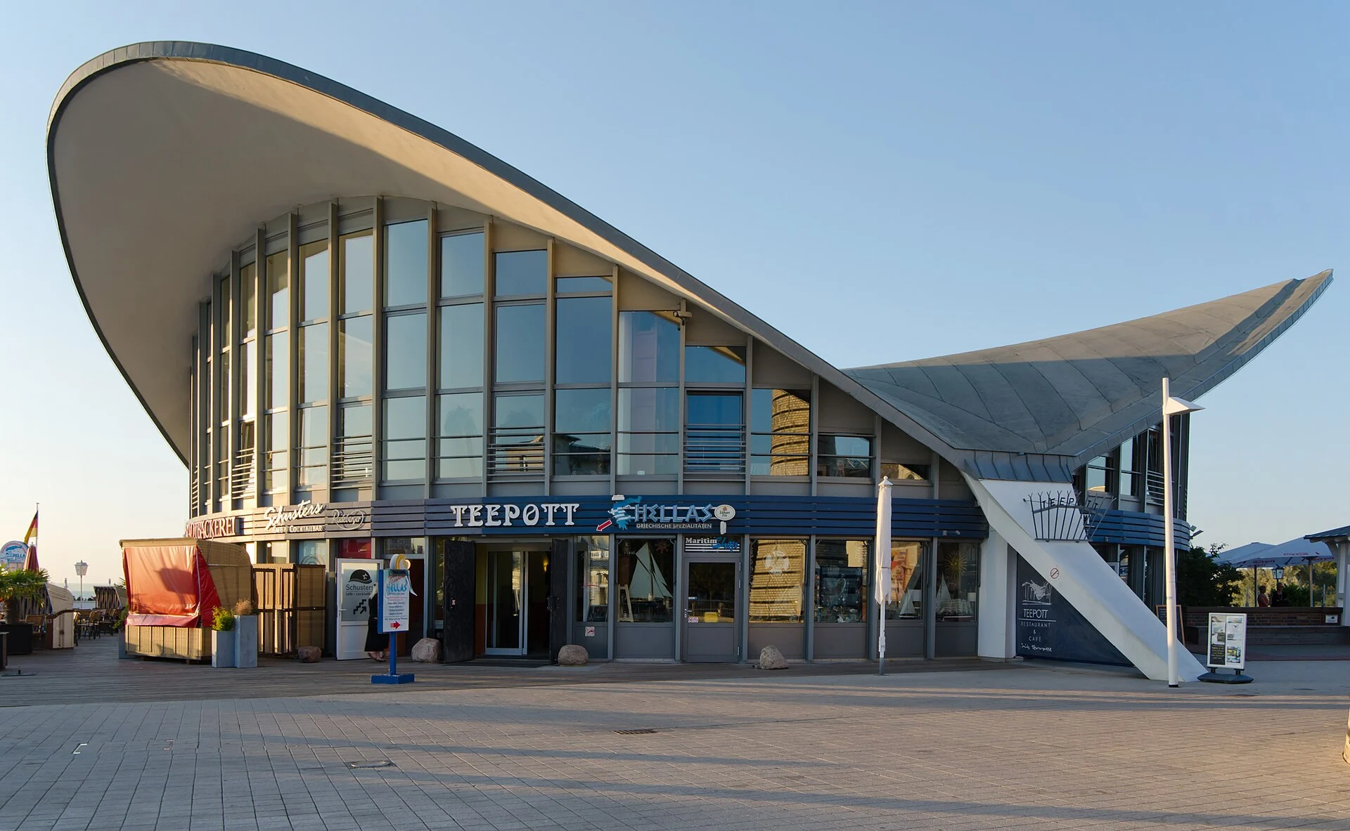 Der Teepott in Warnemünde mit seinem geschwungenen Hyparschalendach und dem Schriftzug „Teepott“ über den Schaufenstern.
