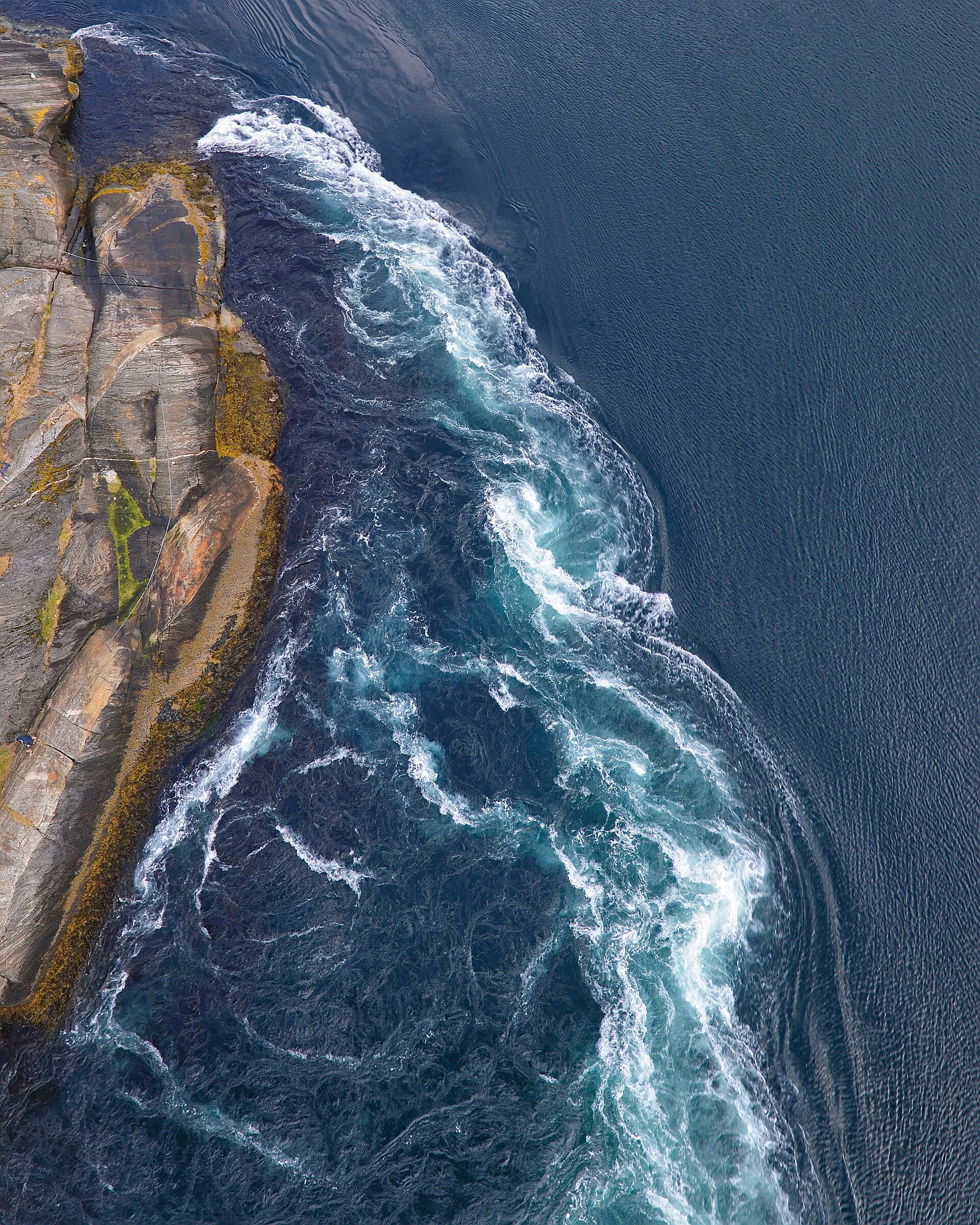 Senkrechte Luftaufnahme der schäumenden Gezeitenströmung des Saltstraumen bei Bodø entlang eines Felsufers.