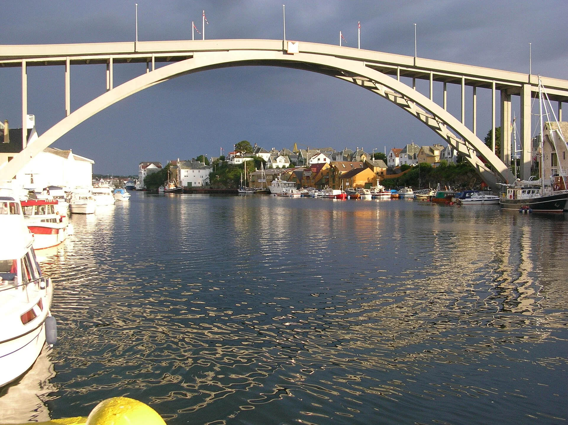 Blick über das Smedasundet in Haugesund unter dem Bogen der Risøybrua hindurch, mit Booten an den Kaikanten.