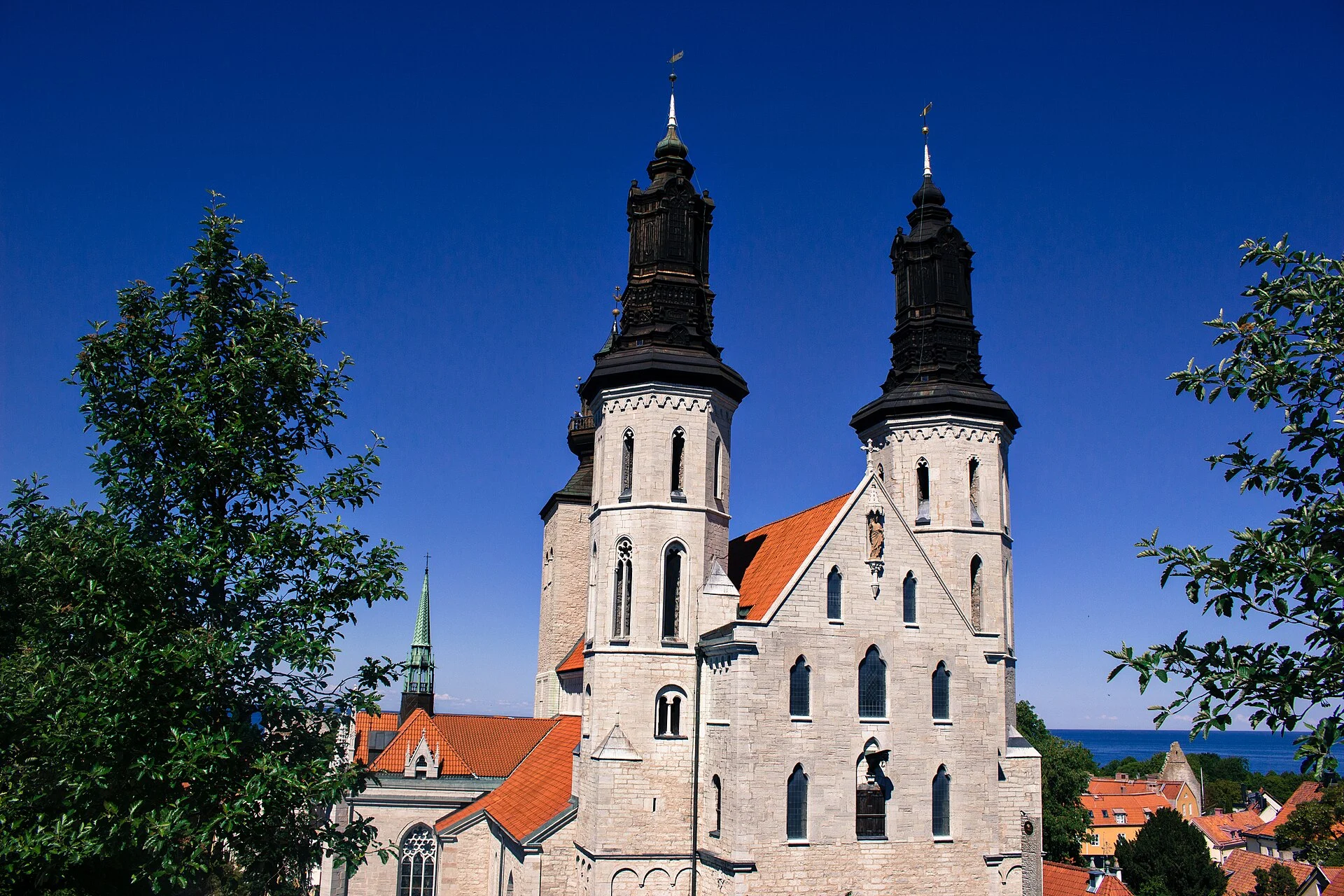 Außenansicht des Doms St. Maria in Visby mit den charakteristischen Türmen vor blauem Himmel und Ostsee im Hintergrund.