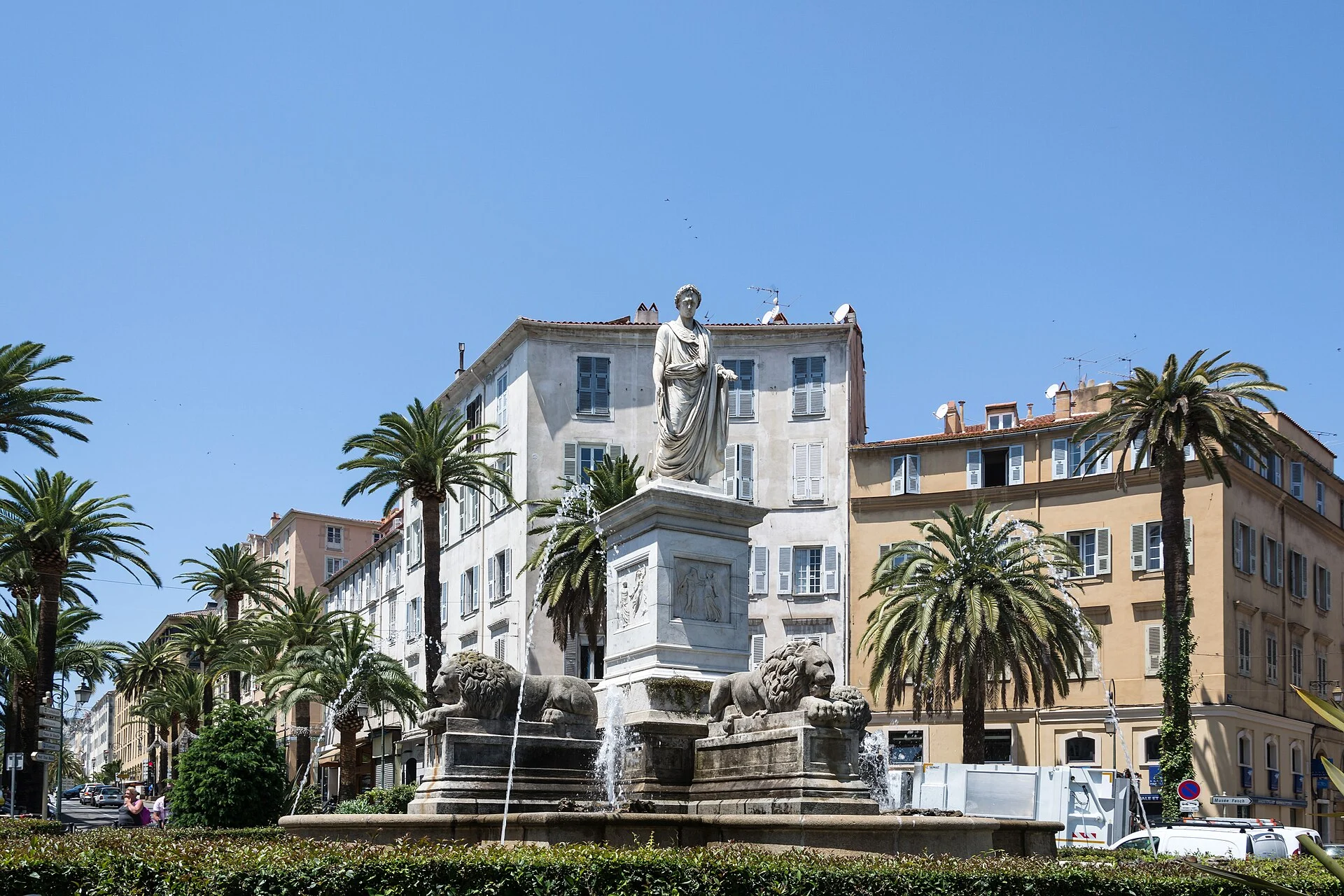Die Place Foch in Ajaccio mit Palmen, Häuserzeile und dem Napoleon-Denkmal über dem Brunnen
